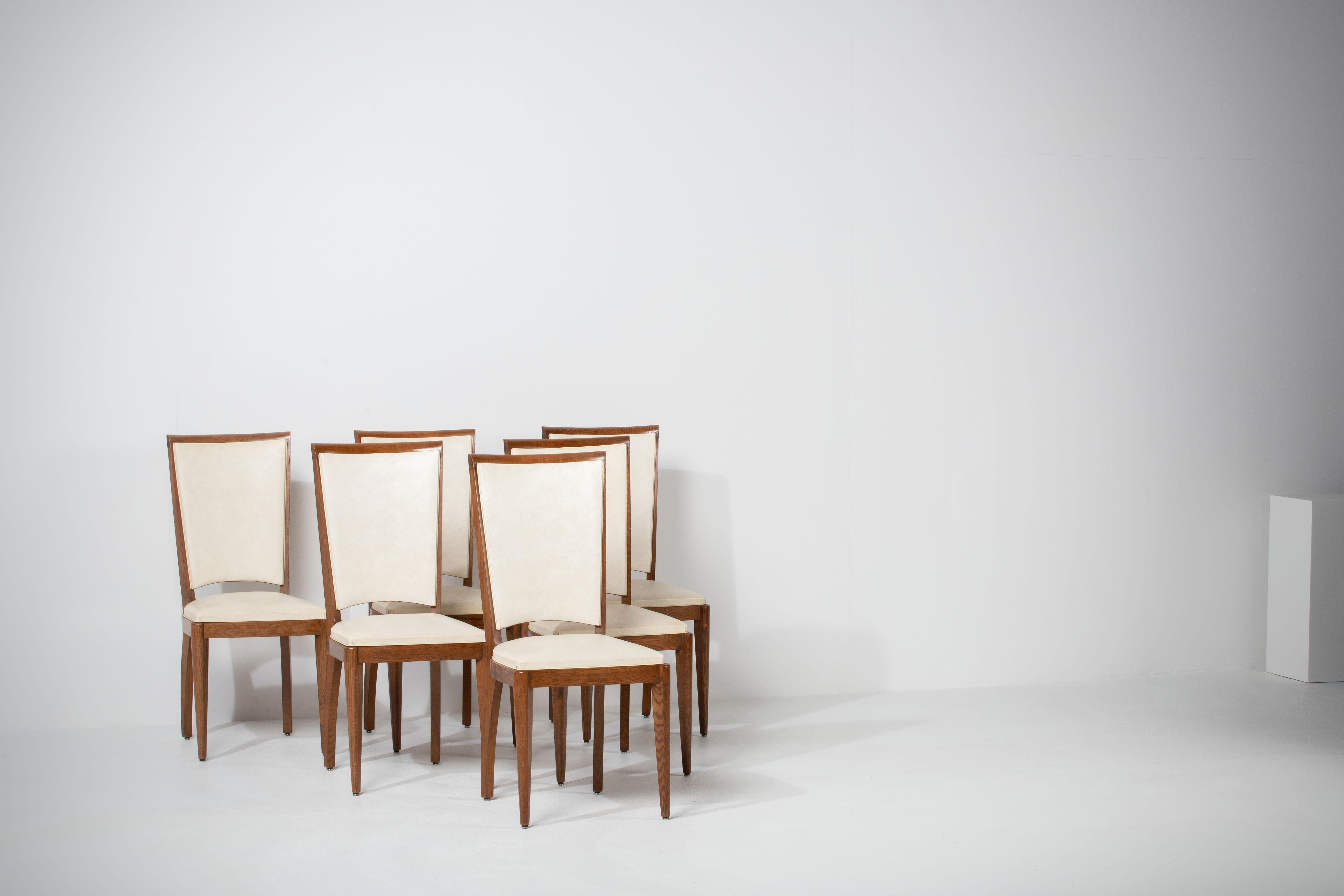 Set of six upholstered high back chairs covered in yellow vynil, exhibiting traditional French design elements in a deep oak finish.

In the style of René Prou, Albert-Lucien Guenot, Pomone, André Arbus, Baptistin Spade, Charles Dudouyt, Herman