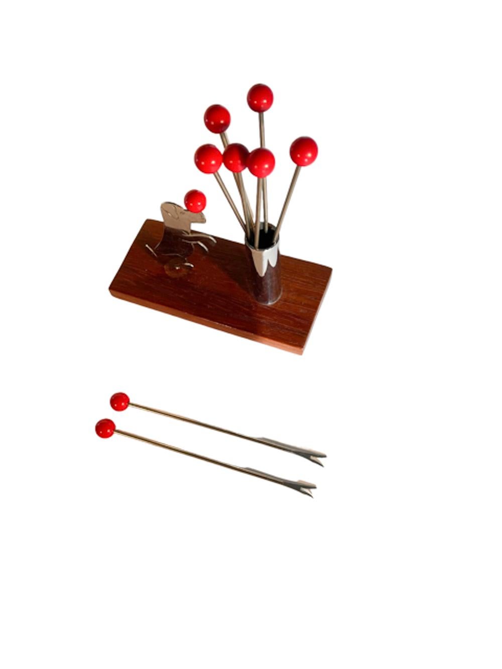 Art Deco cocktail pick set having a chrome cylinder on a wood base holding 8 ball-topped picks with forked tips next to a chrome figure of a dog sitting up and balancing a ball on its nose.