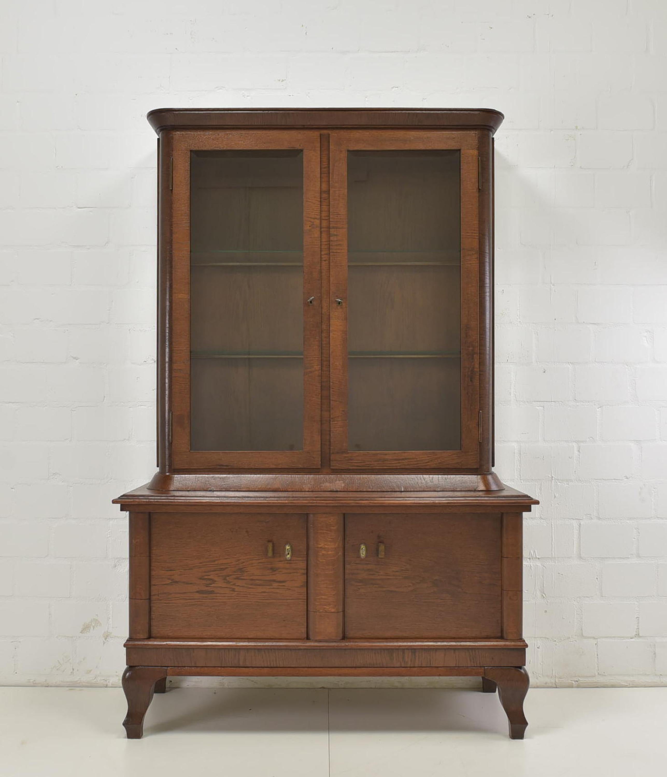 Showcase restored Art Deco around 1930 oak showcase

Features:
Three-sided glazed display case on two-door base
Original glazing with facet cut
Beautiful patina
The cabinet is in two parts (upper / lower part)

Additional