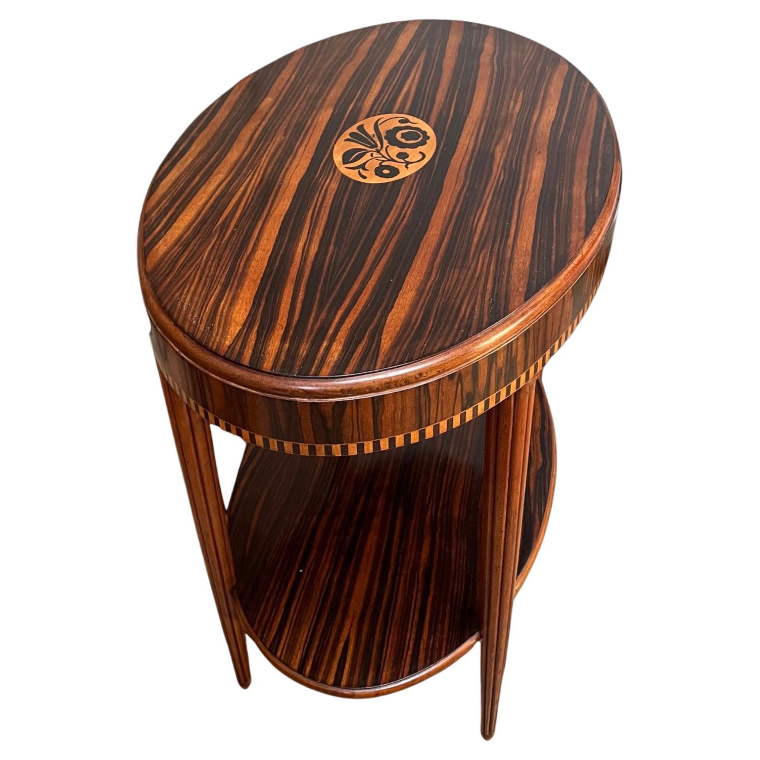 A quality French Art Deco side table in macassar ebony and walnut. Oval, with the top inlaid with a central floral motif and a shelf below. Raised on four elegantly turned and tapered reeded legs
All our furniture is professionally polished and