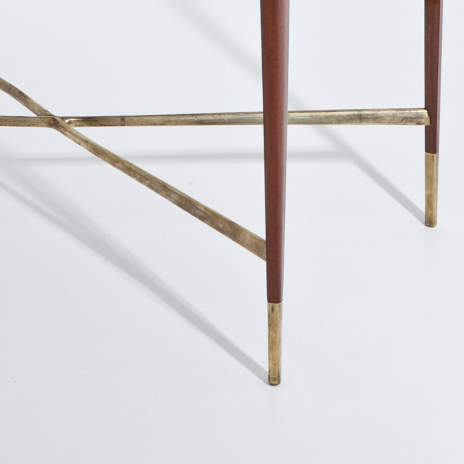 Side table standing on tall tapered legs with a rectangular tabletop and a mirrored veneer pattern. The legs have brass caps and an x-shaped strutting between them.