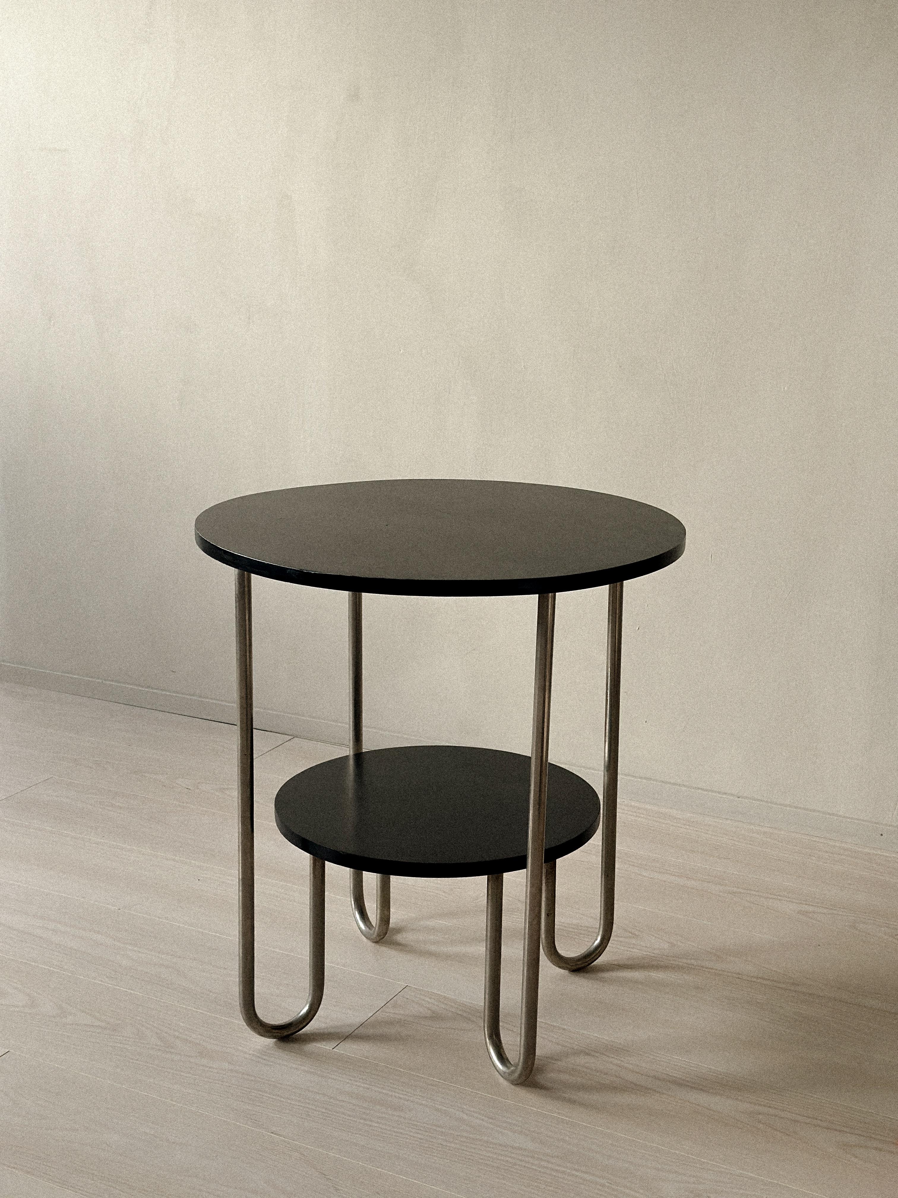 Side table from the 1930s with a two-plane design. The base has turned legs, and the structure features tubular steel. The tabletop includes a tray marked Böhlmarks. Wear constant with age and use.