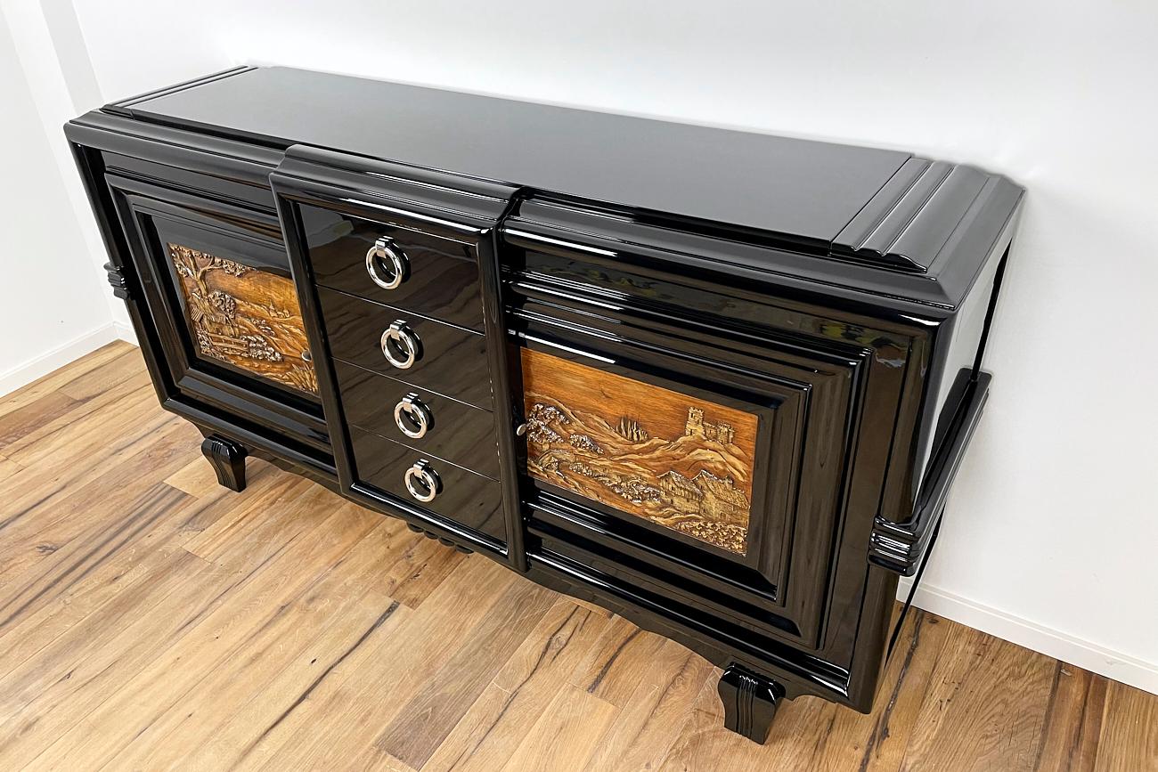 This sideboard from France was previously completely made of oak. We painted the body in black piano lacquer. The curves with the light reflections already come into their own and frame the two paintings on the fronts stylishly. The entire piece of