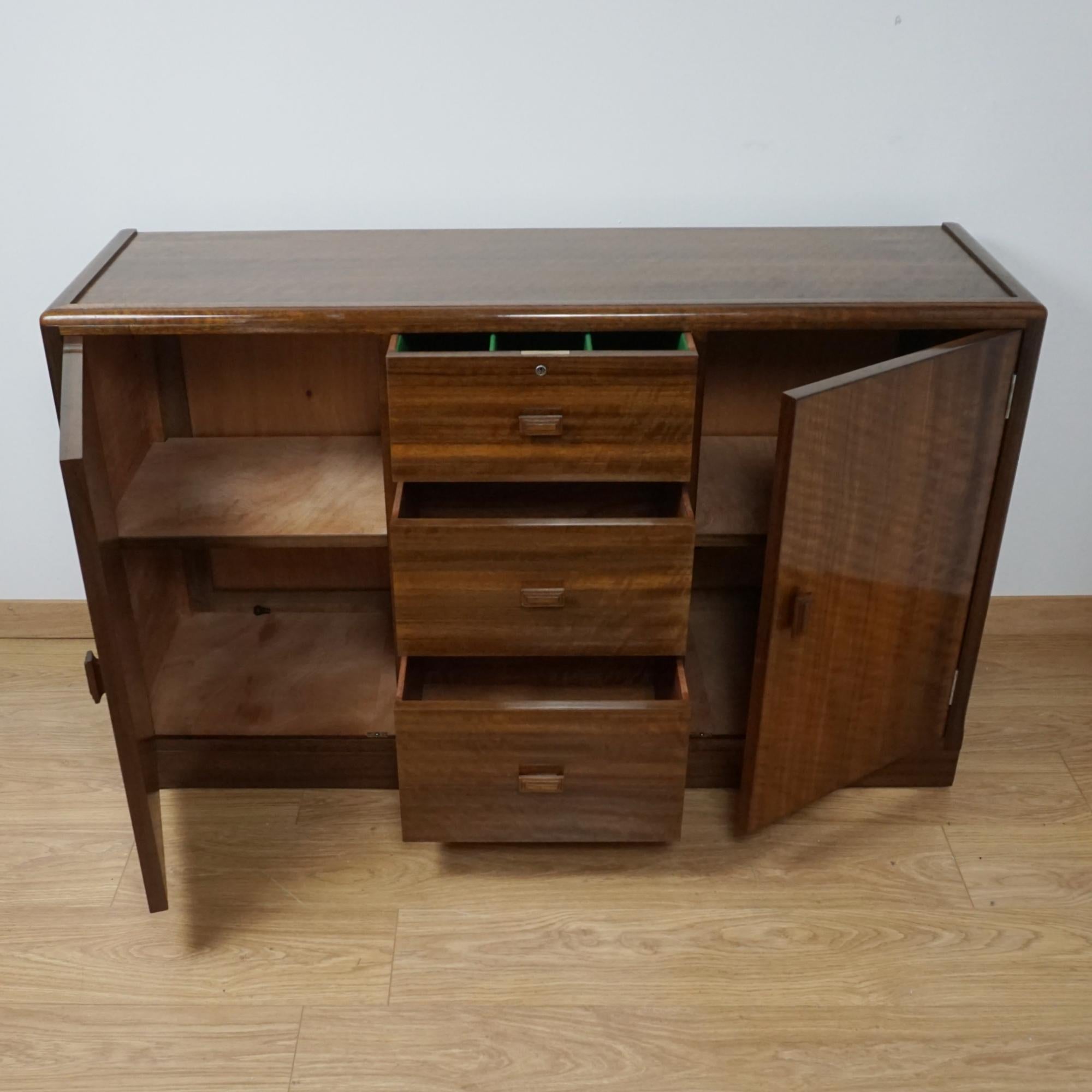 An Art Deco sideboard by Betty Joel. Australian walnut veneered with three central drawers and two shelved cupboards to either side. Glass insert to top. Original walnut handles. 