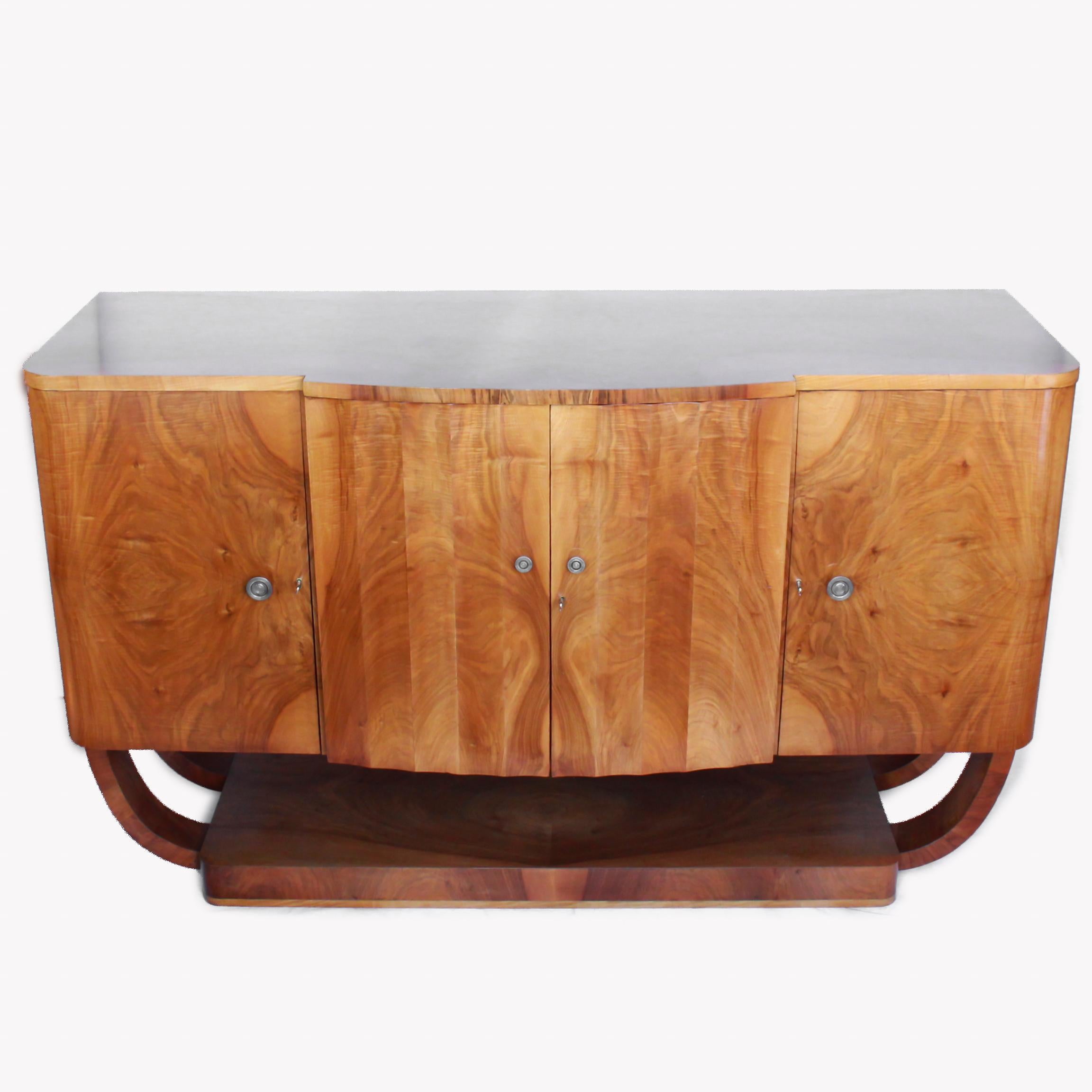 An Art Deco sideboard by Harry and Lou Epstein set over a U-shaped base. Walnut veneer with satinwood banding and original metal handles. Three central drawers with cupboard shelves either side. 

Dimensions: H 97cm, W 1m 60cm, D 58cm

Origin: