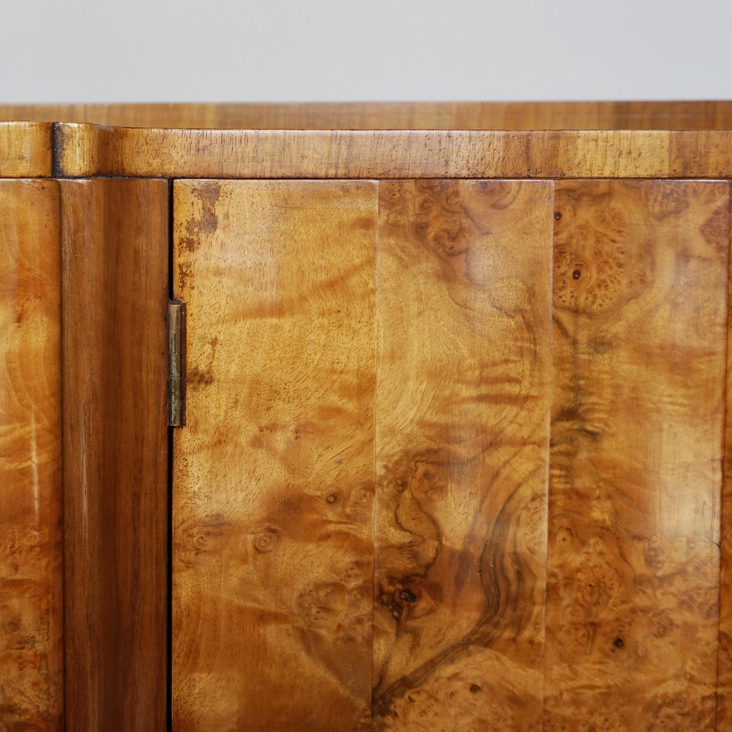 An Art Deco sideboard by Harry & Lou Epstein. Central drawer and bottle storage compartments fronted by fluted burr walnut doors, flanked by two burr walnut fronted shelf compartments. Burr walnut veneered to top, with figured walnut to sides and