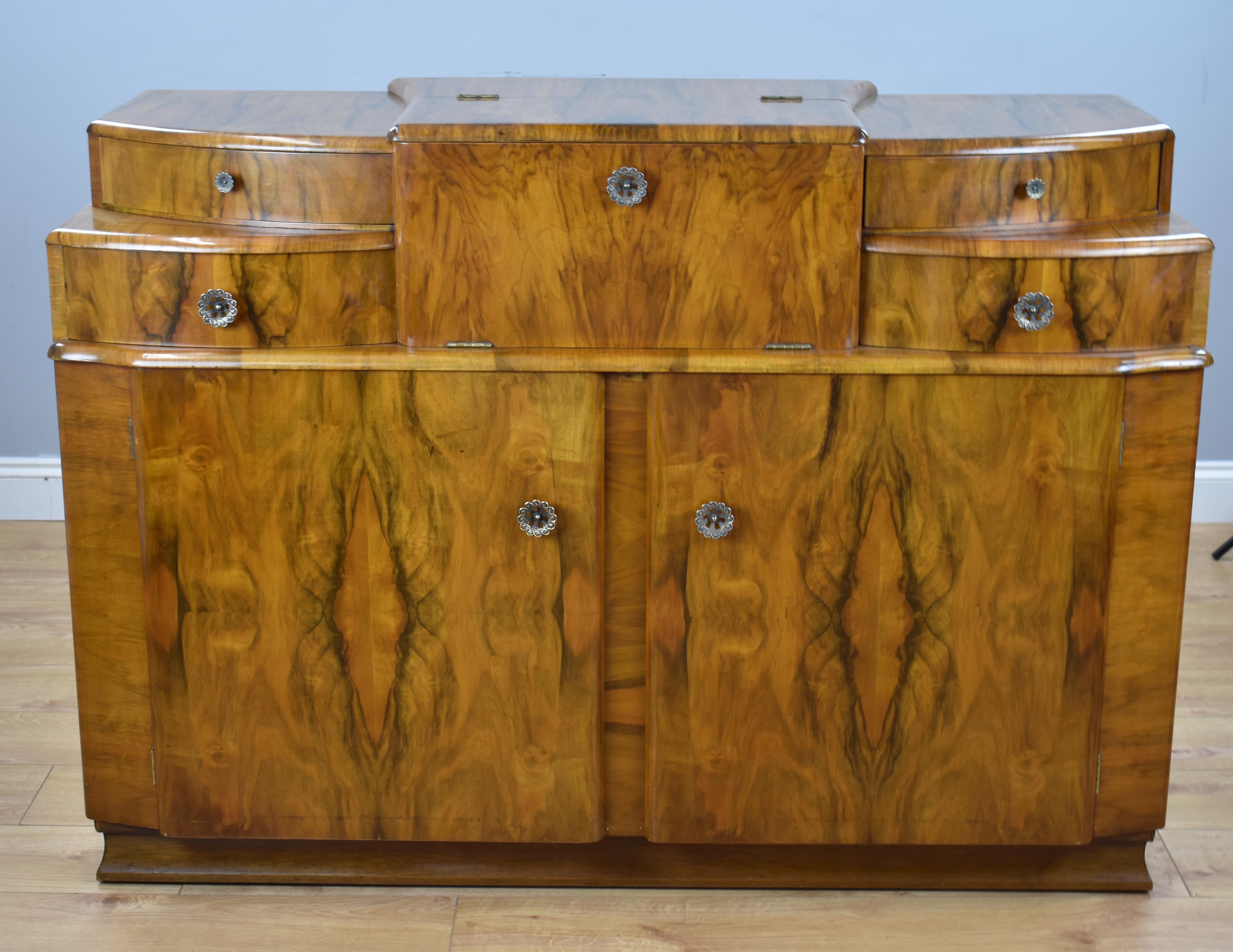 Art Deco walnut sideboard/cocktail cabinet in good condition having been recently hand polished. The sideboard has a lift up top to the centre revealing cocktail sticks and lemon squeezer with mirrors top and bottom, either side has a pullout /