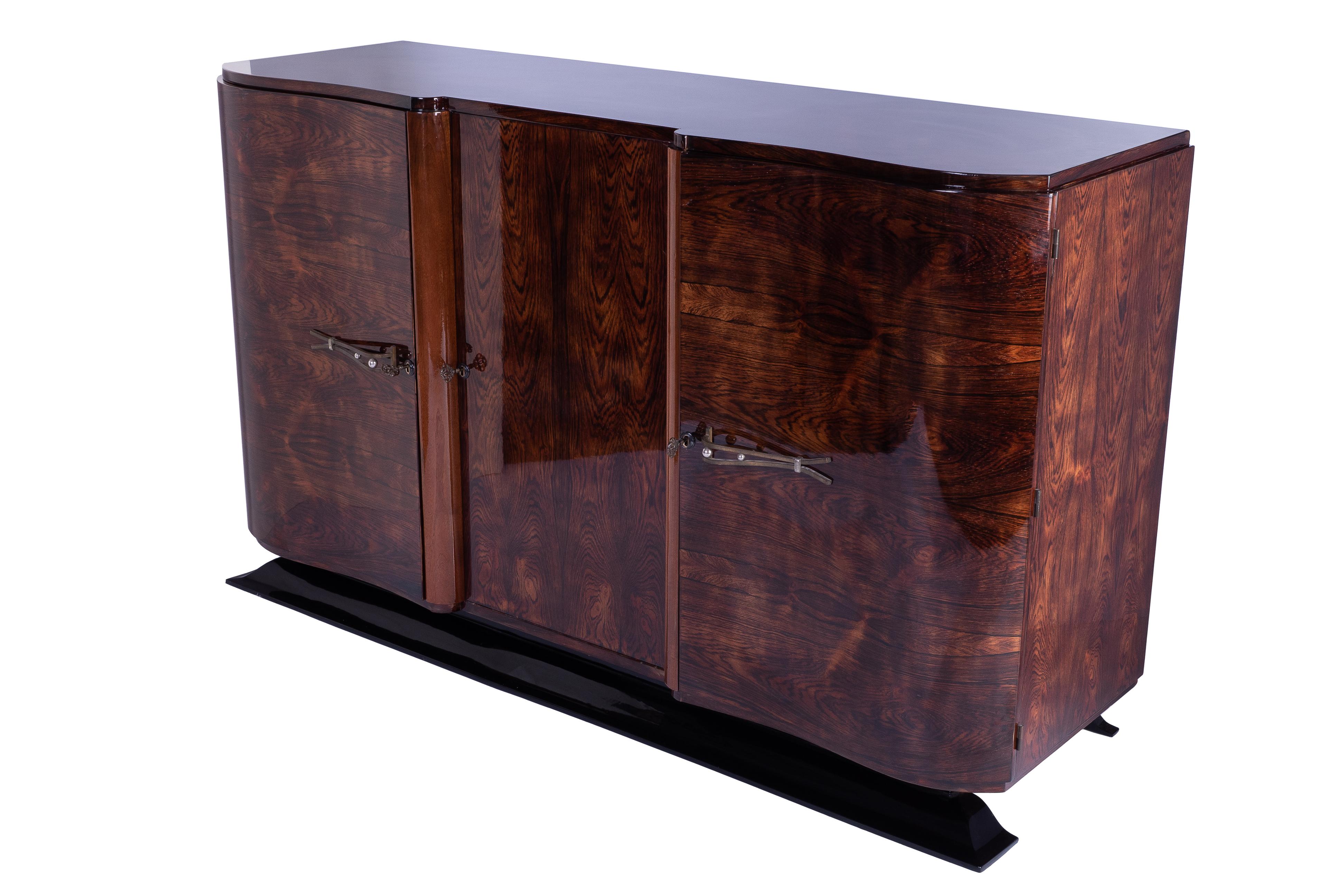 Art Deco sideboard / credenza featuring a solid mahogany frame veneered in luxurious rosewood and finished in a high gloss lacquer. The piece has two single side doors with original brass hardware. Plenty of storage. French foot stained in a darker