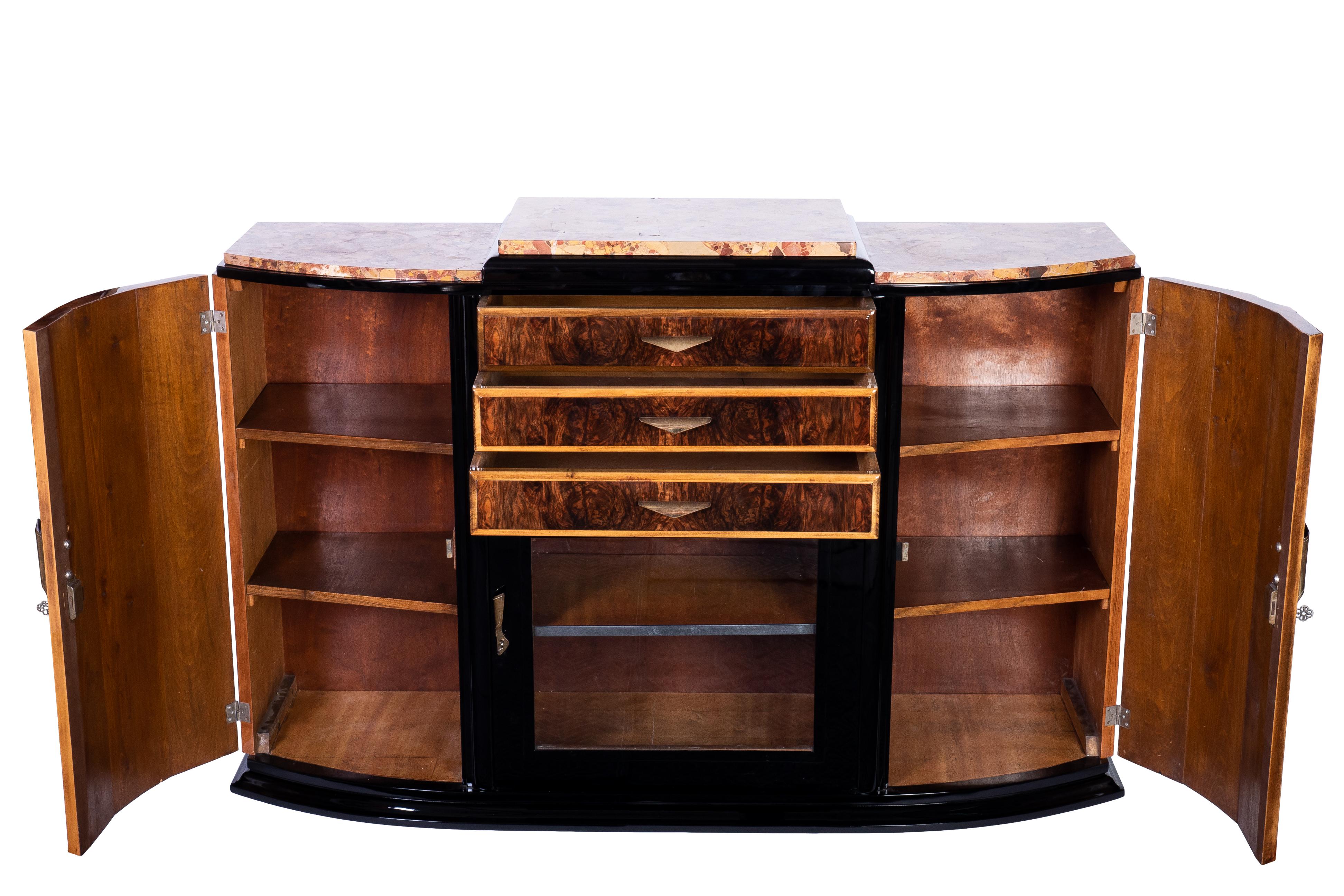 Art Deco sideboard, credenza or showcase featuring a solid mahogany frame veneered in luxurious walnut and finished in a high gloss lacquer. The piece has two single curved side doors, one center display and three center drawers . Plenty of storage.