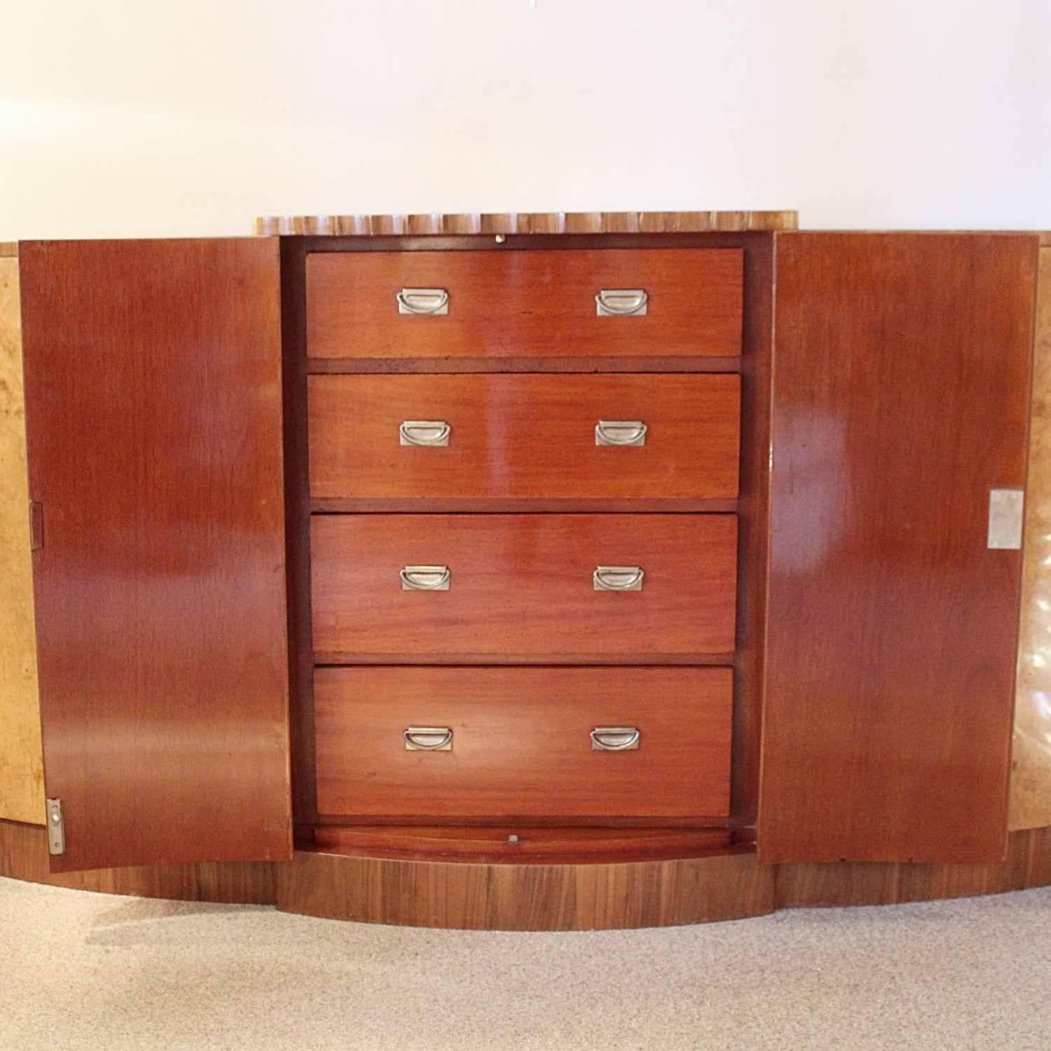 An Art Deco sideboard by Harry & Lou Epstein. A fluted front central cabinet opens to mahogany lined drawers, with shelved cabinets either side with top drawers. Original bakelite handles.

Burr walnut with straight grain walnut banding.

 