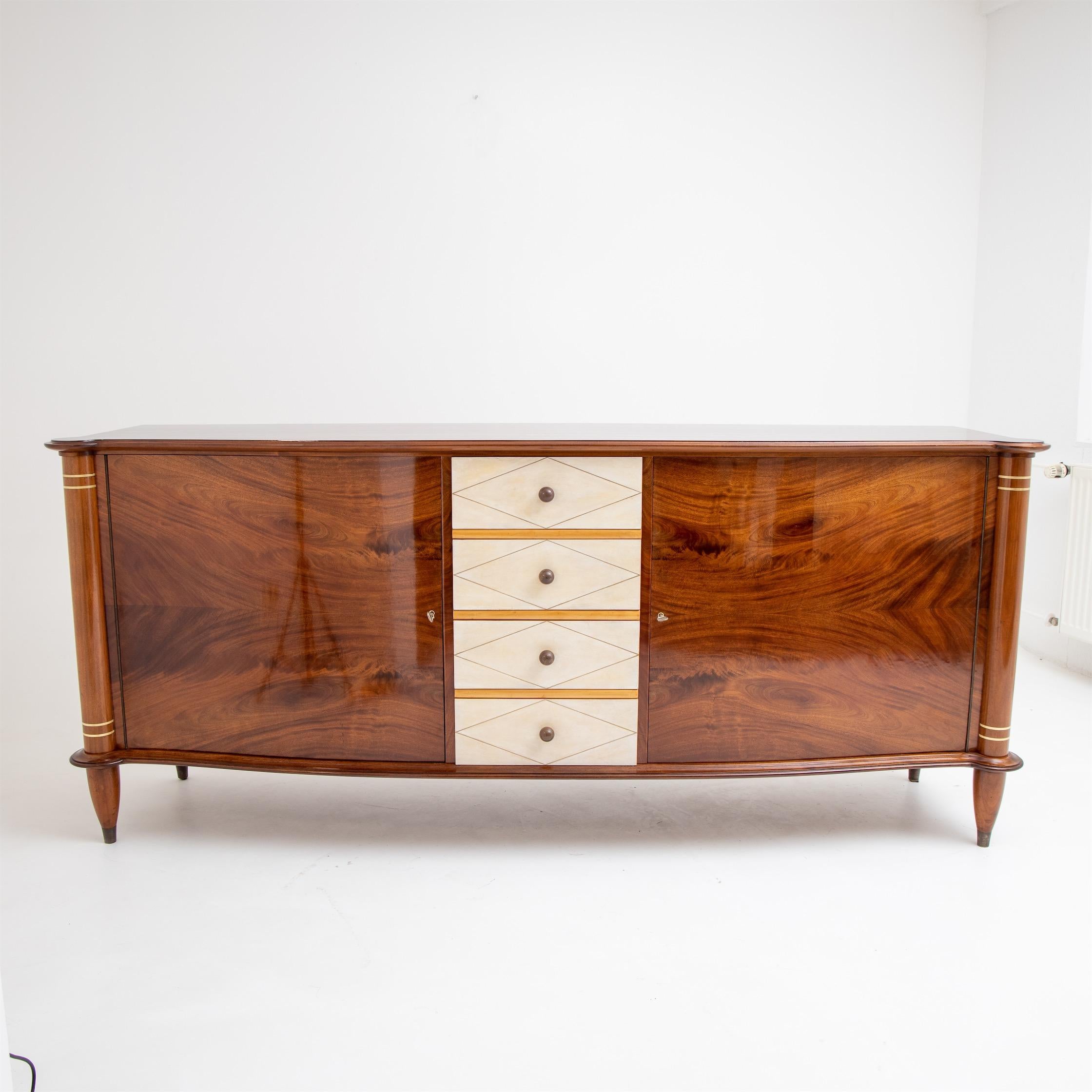 Three-door sideboard in the style of Leleu with brass profiles and rounded corners. The body is veneered in mahogany and has a gently curved bow front. The sideboard has been expertly restored and hand polished.