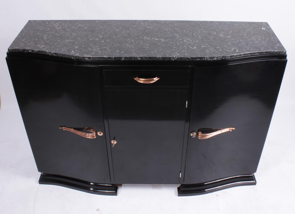Art Deco sideboard in piano lacquer, circa 1930.
a large art deco sideboard finished in ebonised piano lacquer with copper plated handles and a black and white marble top, the sideboard has three lockable doors with a shelf behind and a single top