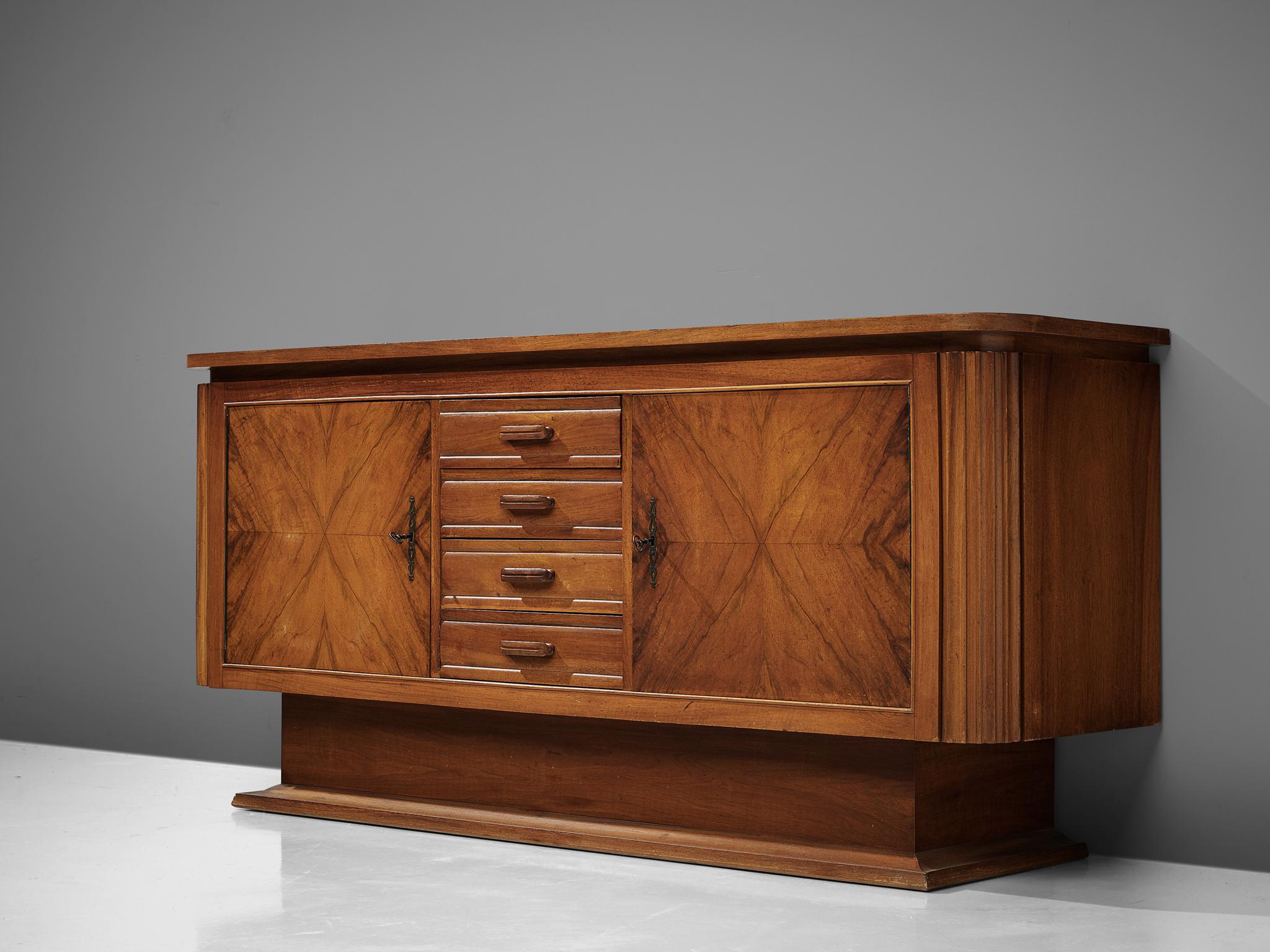 Sideboard, walnut, iron, Europe, 1950s

This sturdy pedestal sideboard features two doors and four drawers on the front. The doors are finished with beautiful book-matched walnut veneer and decorative iron locks. The corners are rounded and contain