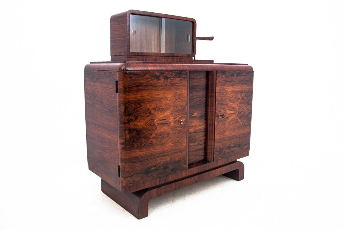 Art Deco sideboard, Poland, 1950s.

The sideboard has a small extension with sliding glass doors and an external profiled shelf. The lower part of the furniture has one shelf. Functional sideboard that will work great in the living room as a