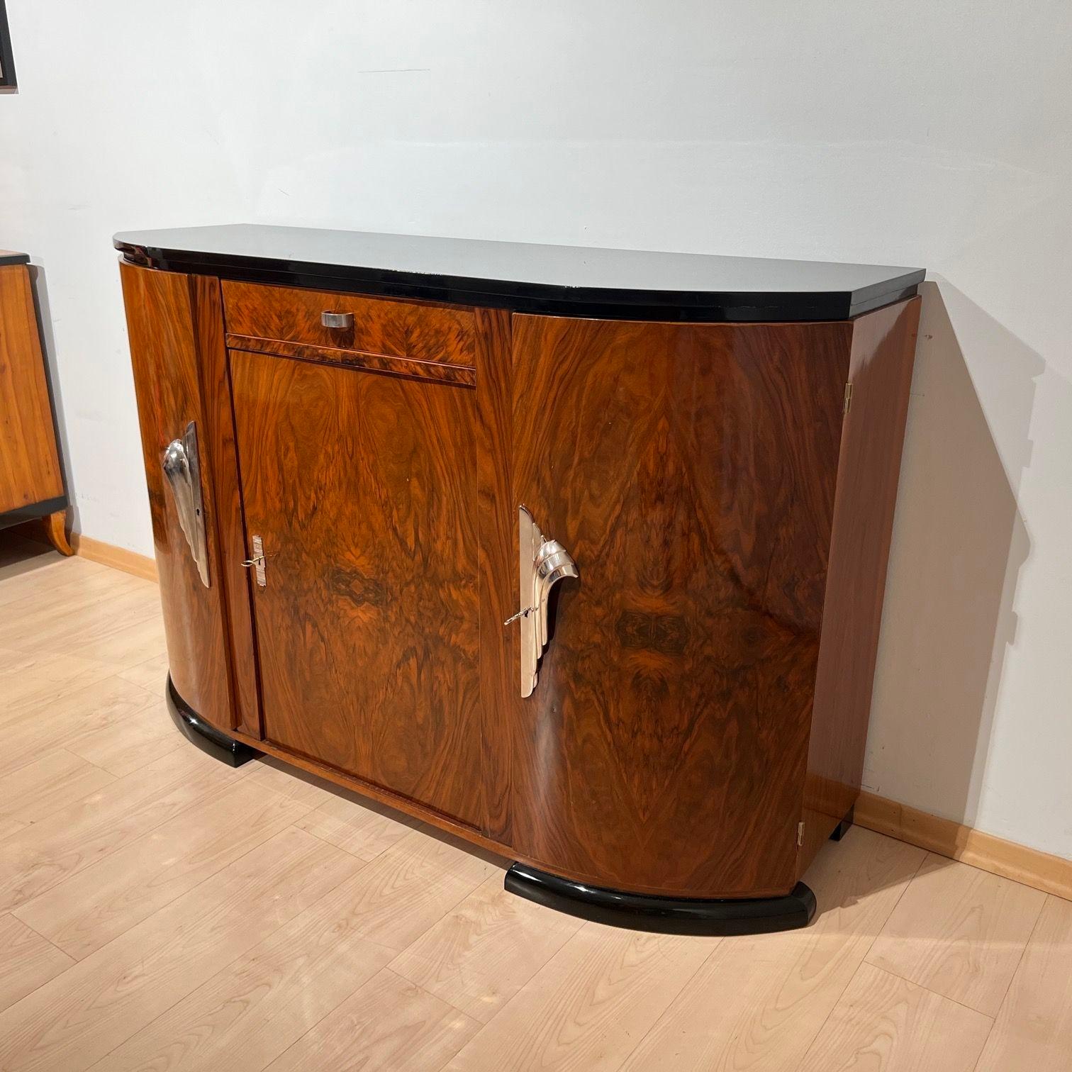 Small Art Deco Sideboard or buffet with curved front from France around 1930.
Beautifully grained walnut veneer, shellac hand-polished.
Nickel plated bronze fittings and key escutcheon. Ebonized legs and top rim as well as black high-gloss lacquered