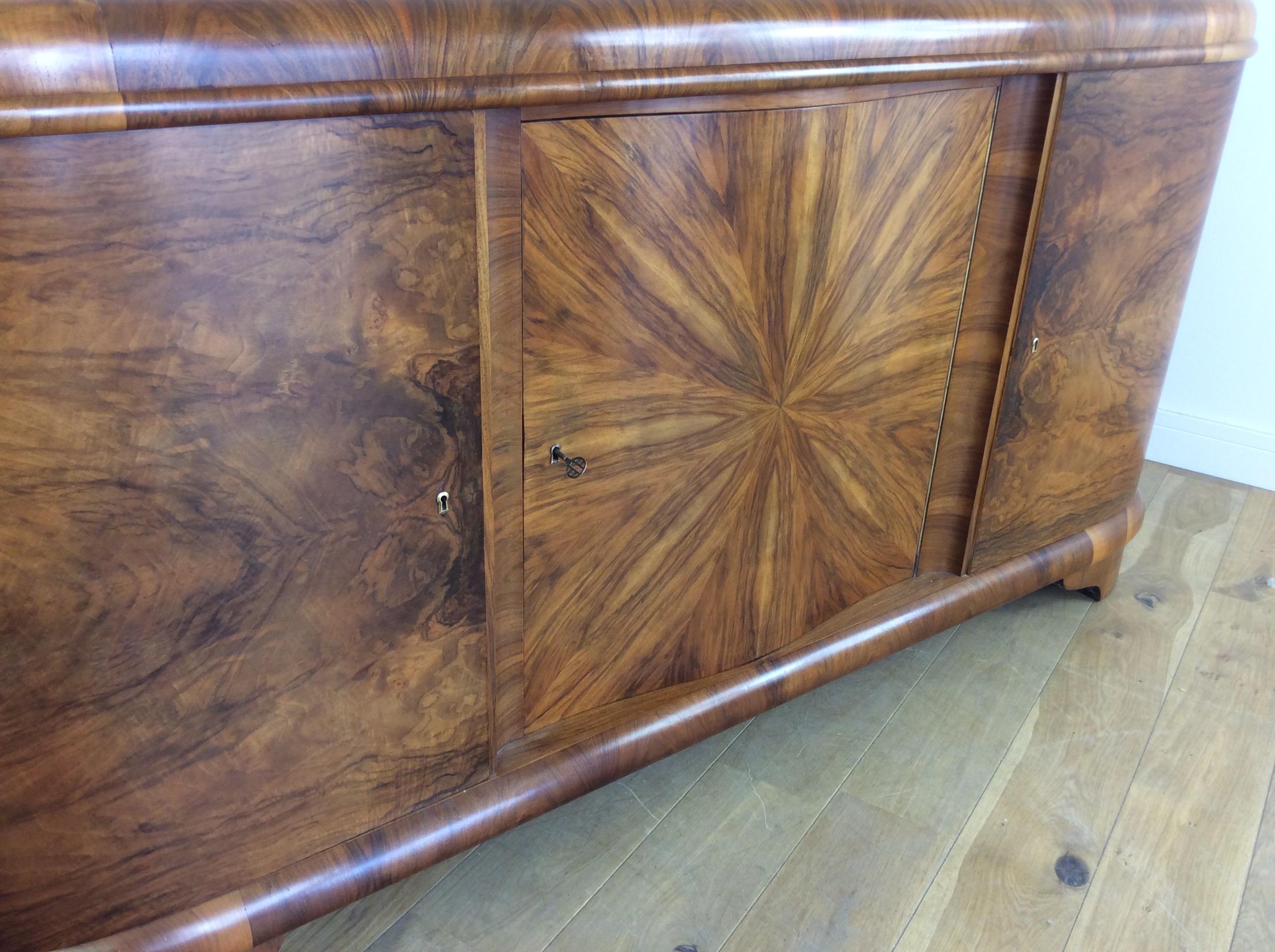 Art Deco large sideboard with impressive figured walnut, the centre panel with fantastic sunburst design.
Centre section fitted with 3 drawers and pullout / pull-out serving shelf with marble centre,
Measures: 110 cm H at the back 101 cm H at the