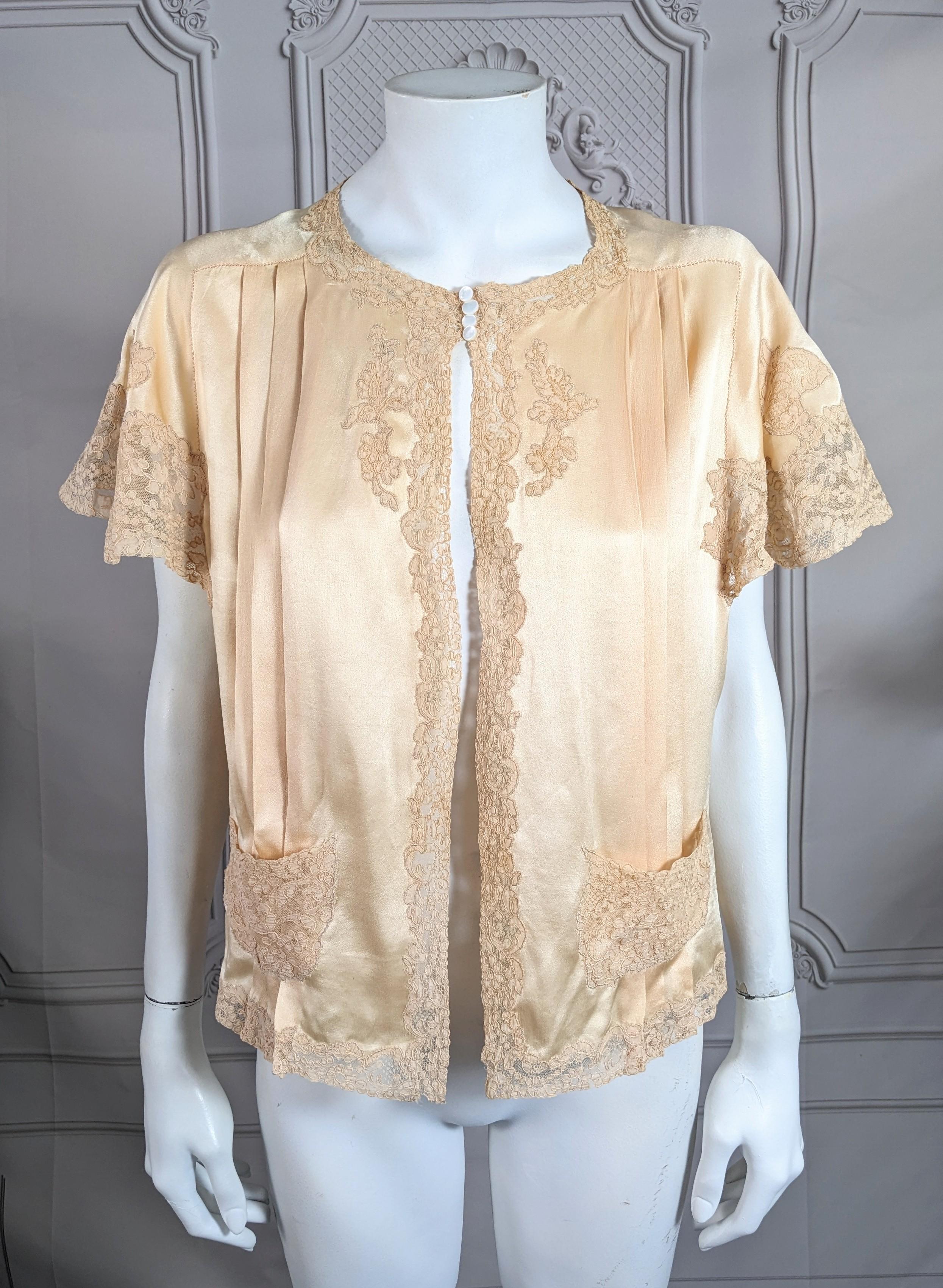 Charmante veste de lit Art déco en satin de soie et dentelle des années 1930. Le satin de soie rose pâle est garni de dentelle d'Alecon dans cette ravissante veste de lit avec des fronces sur le devant. Manches papillon et poches en dentelle beige
