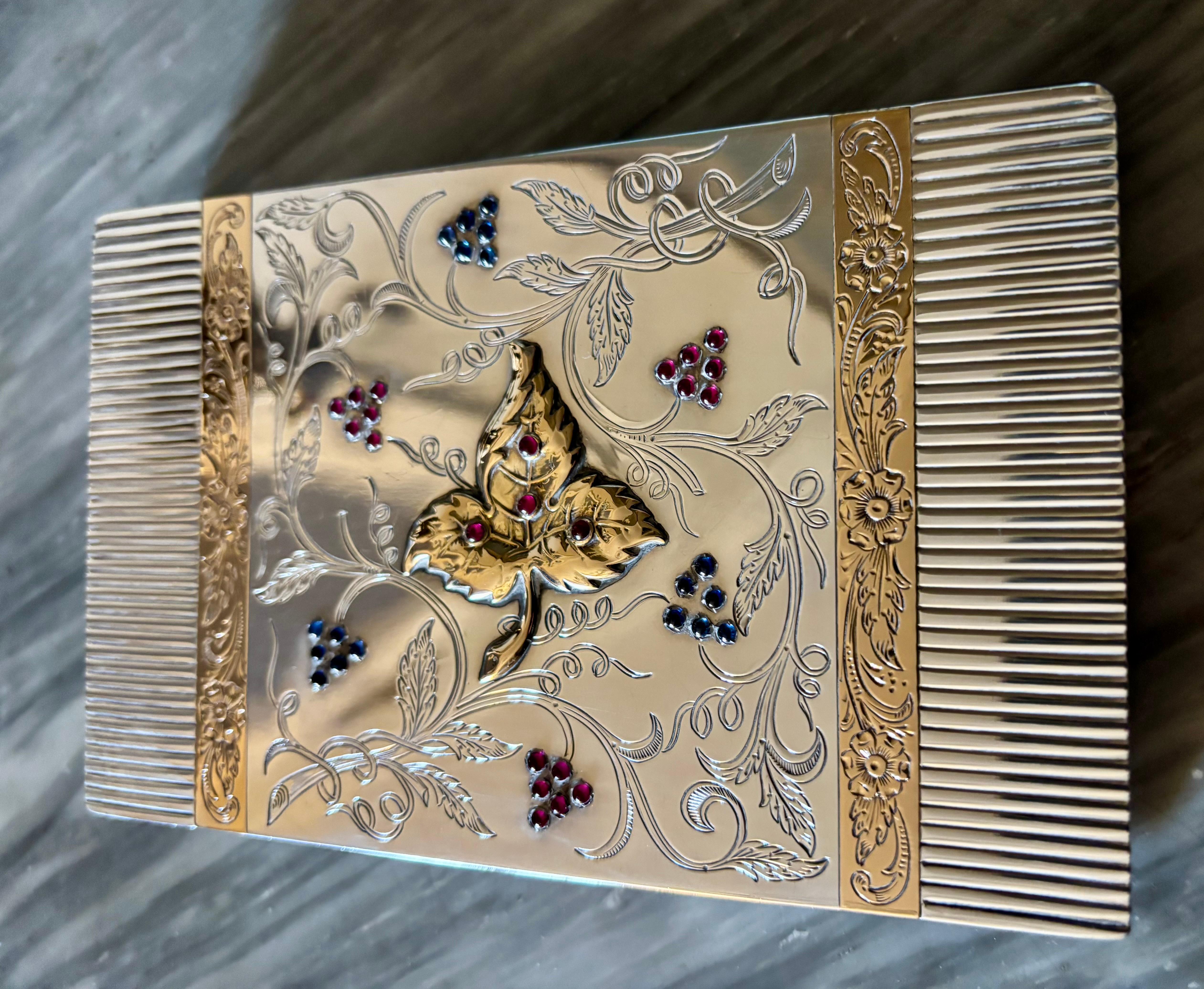 ASTUCCIO DA VIAGGIO ART DÉCO IN ARGENTO E ORO CON GEMME INCASTONATE
Il rettangolo d'oro  e cofanetto d'argento dal design a reticolo decorato con motivi geometrici e fiori con zaffiri e rubini rotondi cabochon, che si apre per rivelare uno specchio