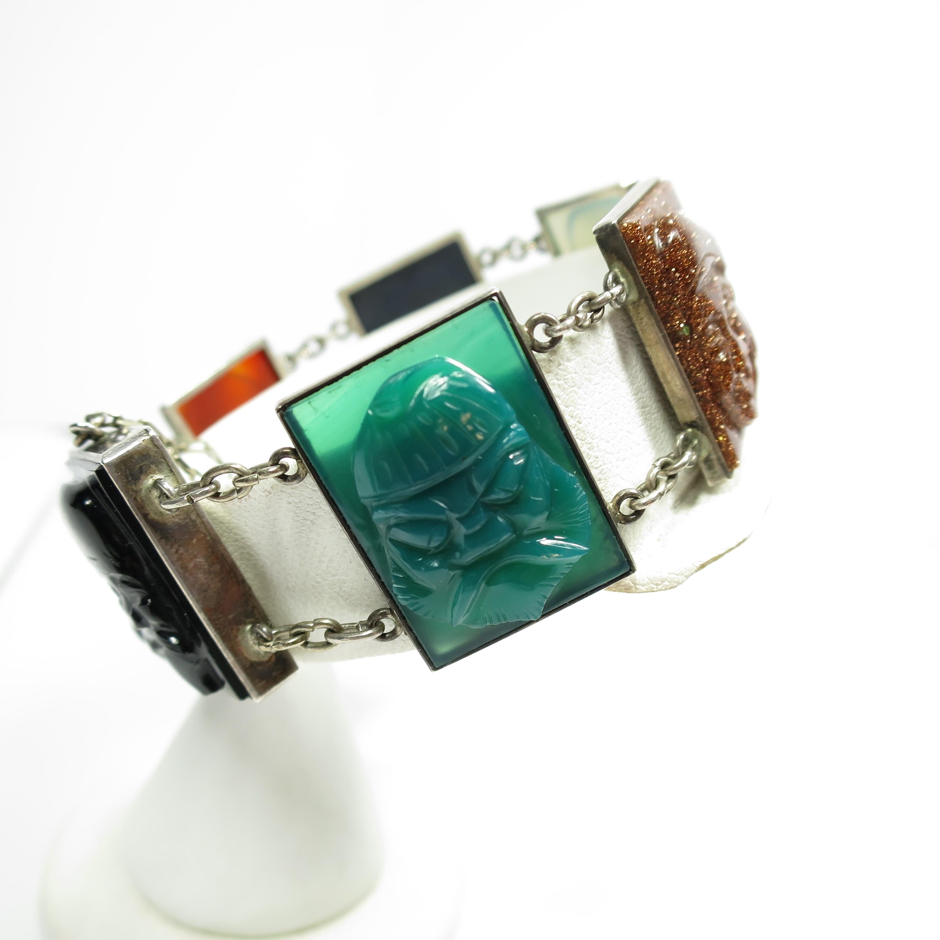Offered here is an Art Deco Chinese silver bracelet with carved semi-precious stones from the 1920s. Narrow rectangular silver frames present open-back bezel-set stones of chrysoprase, carnelian, goldstone, lapis, onyx, and pale lavender jade; the