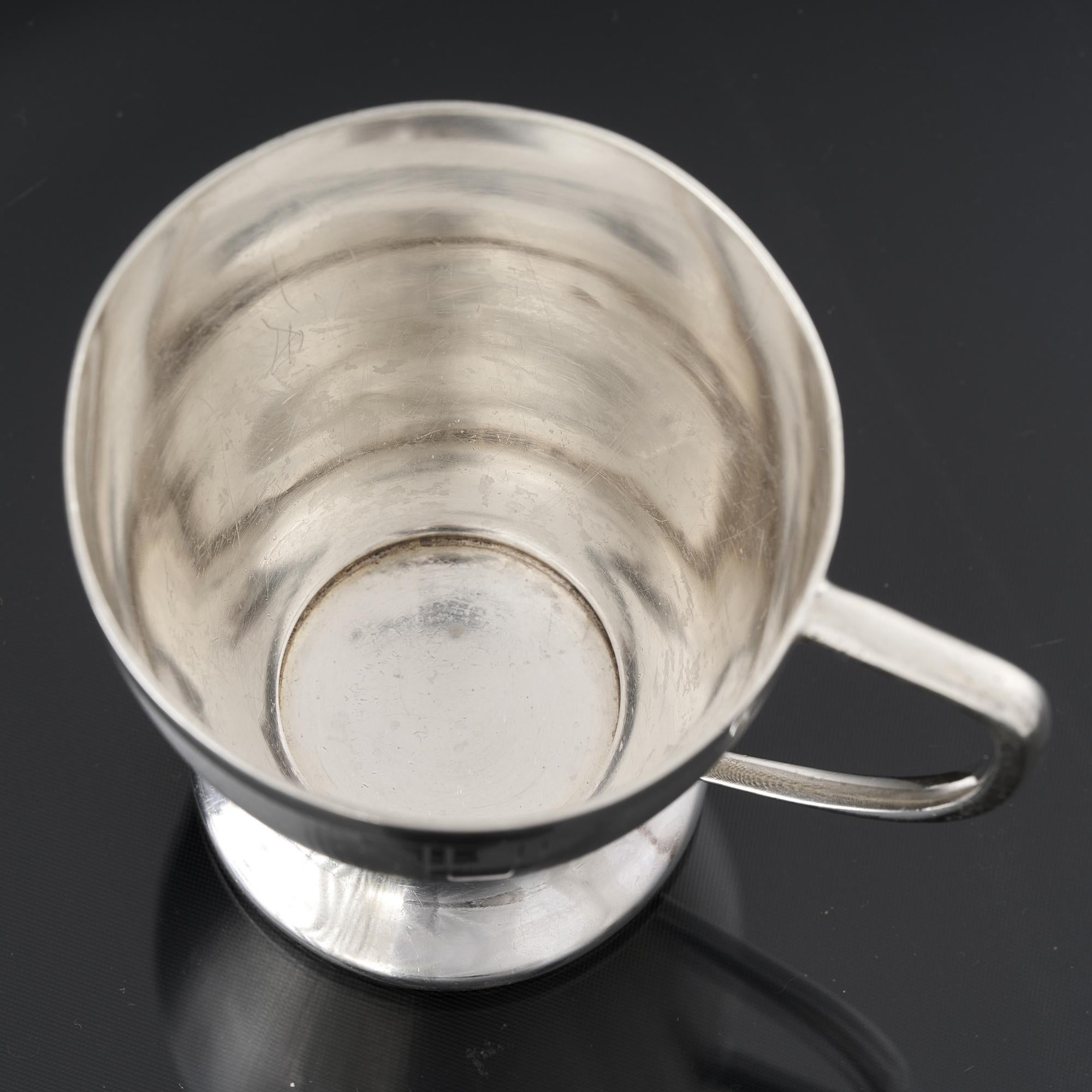 Art Deco style silver child's cup featuring a smart engine turned decoration to the body and plain border lip. The hand engraved, stepped, Art Deco motifs drop down from the lip and the cup and the simple handle is comfortable to hold.

Art Deco was
