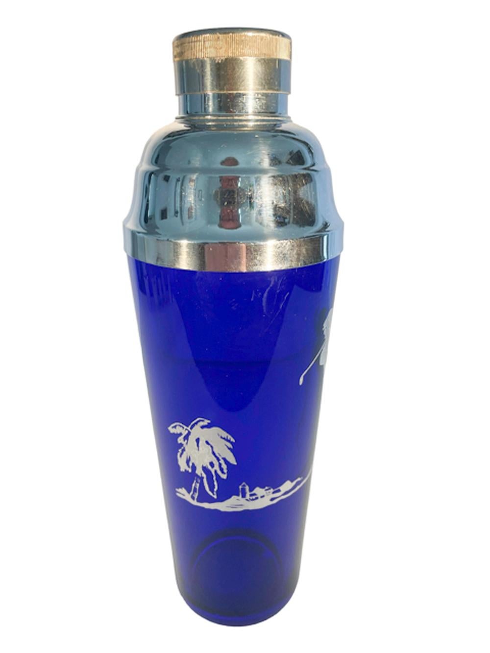 Art Deco silver overlay golf theme cocktail shaker in cobalt glass with a ground foot having buildings on a golf course with a golfer at one end and a palm tree at the other. Topped with a domed chrome center pour lid with integral strainer.