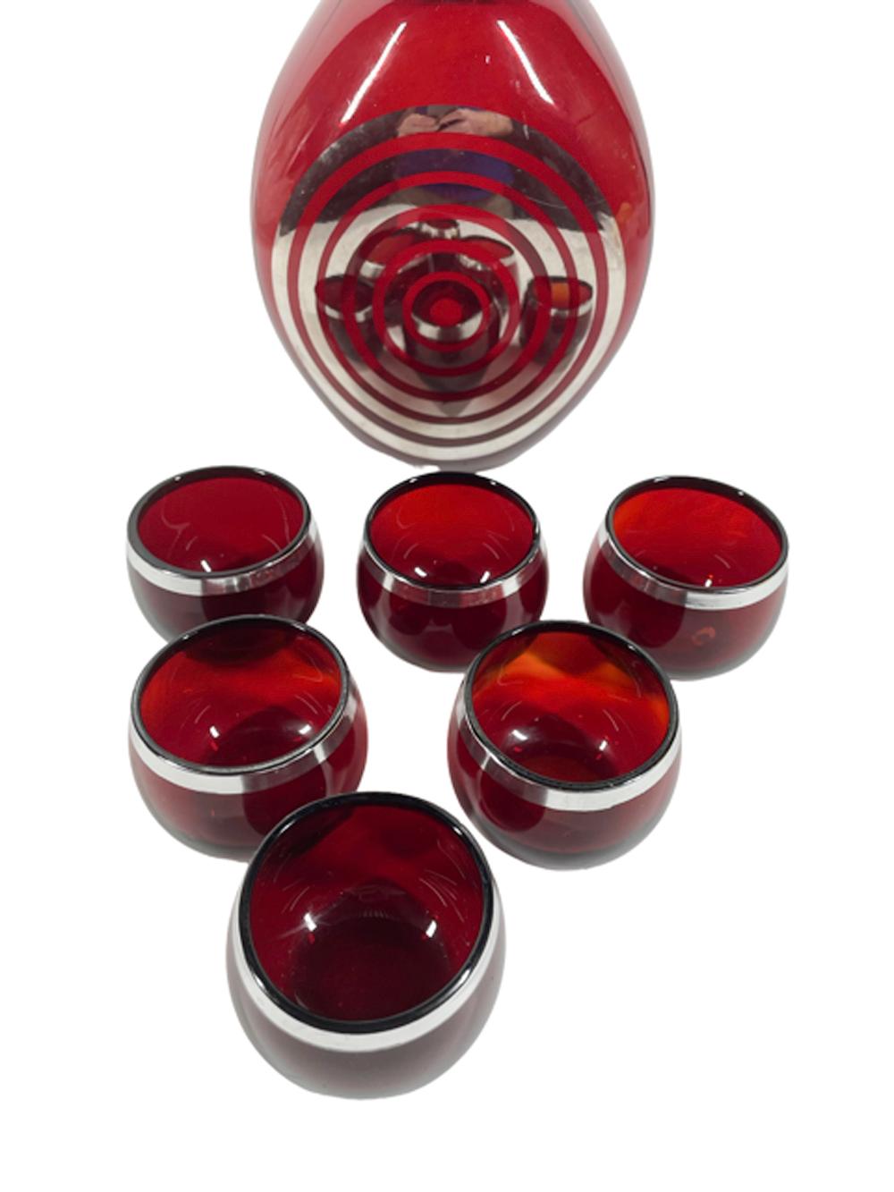 Art Deco silver overlay ruby glass pinch decanter and six roly poly glasses. The decanter with two dimpled sides and mirror finished silver overlay concentric circles on the third. The rim of the decanter as well as the top of the mushroom stopper