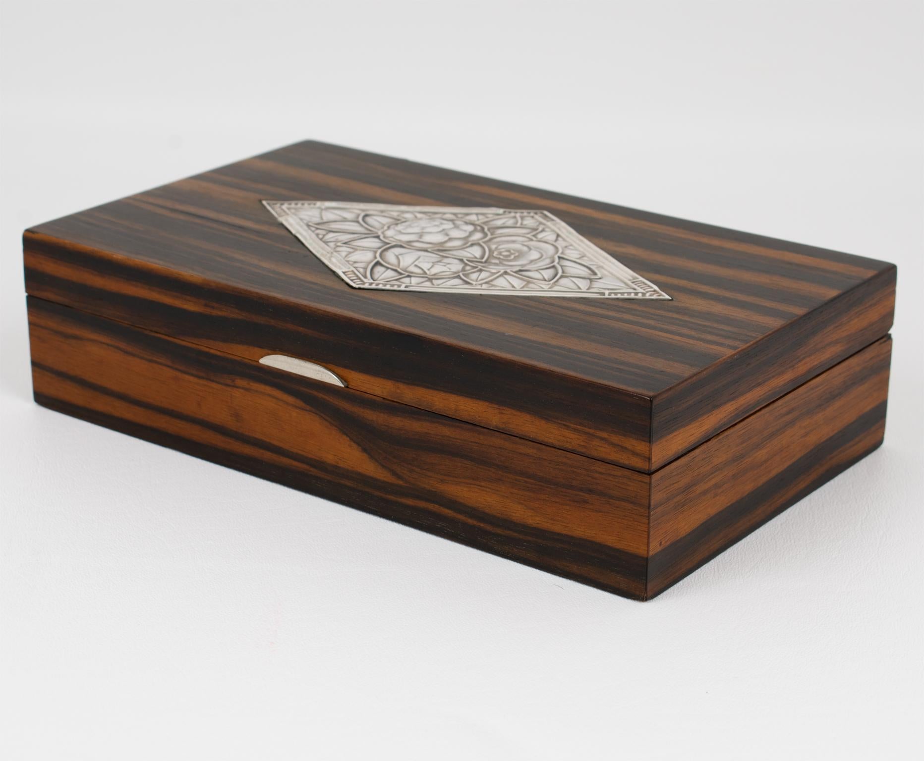Se trata de una elegante caja Art Déco de chapa de plata y tapa de madera fabricada a mano en Francia en la década de 1930. Su forma rectangular presenta una composición refinada, con un cuerpo de madera de Macasar adornado con un asa de metal