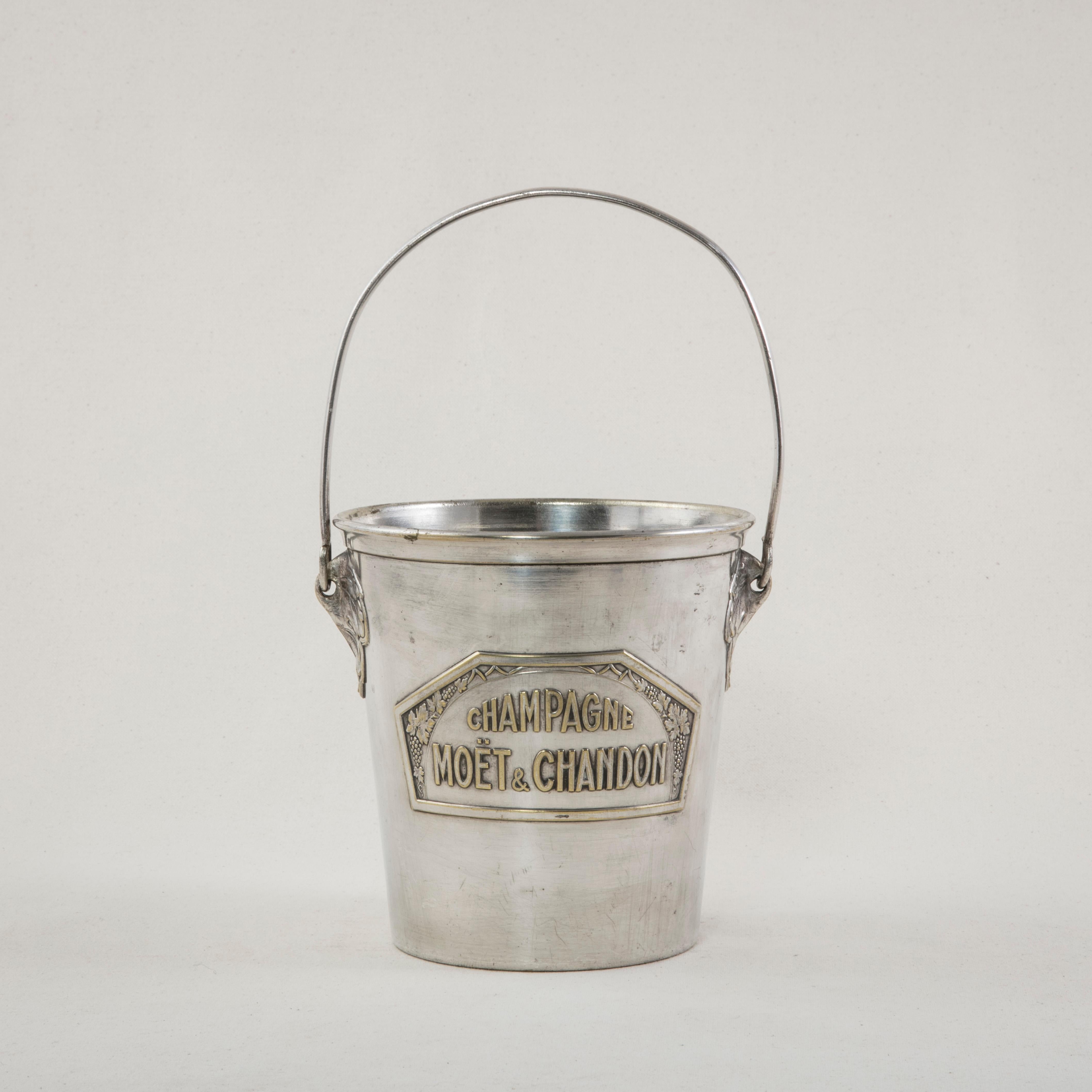 This small scale silver plate ice bucket with handle is from the 1930s and features an Art Deco motif surrounding the renown French champagne name of Moet et Chandon. It is stamped on the bottom Argit Paris. A charming champagne bucket ready to