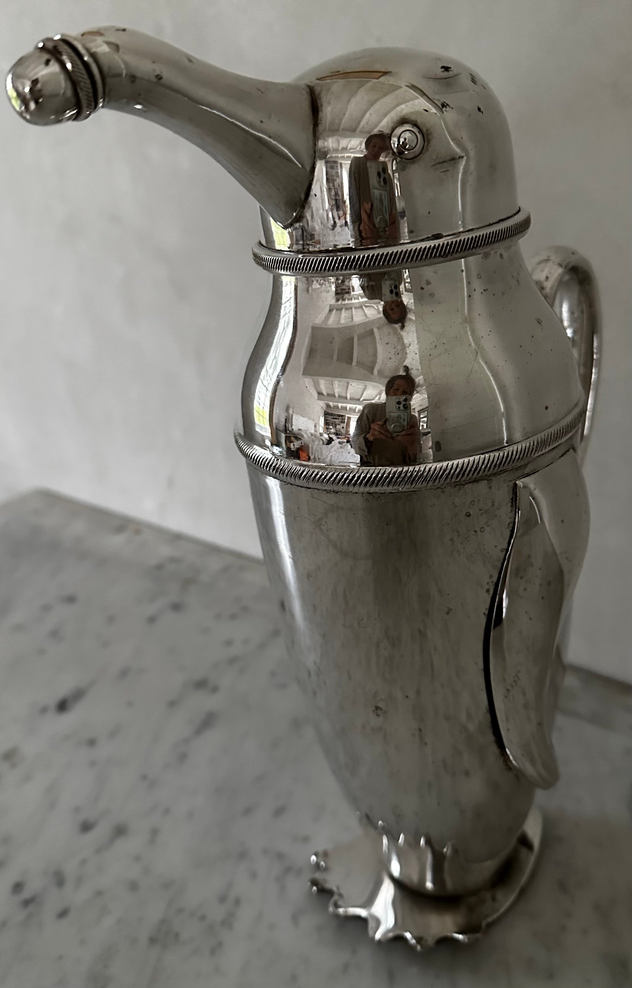 Wonderfully charming silver plated cocktail shaker,  bar or water pitcher in the form a penguin with a screwed on cap at the end of the spout and the head that lifts off for filling.  The pitcher sits on penguin feet making it extra special and a