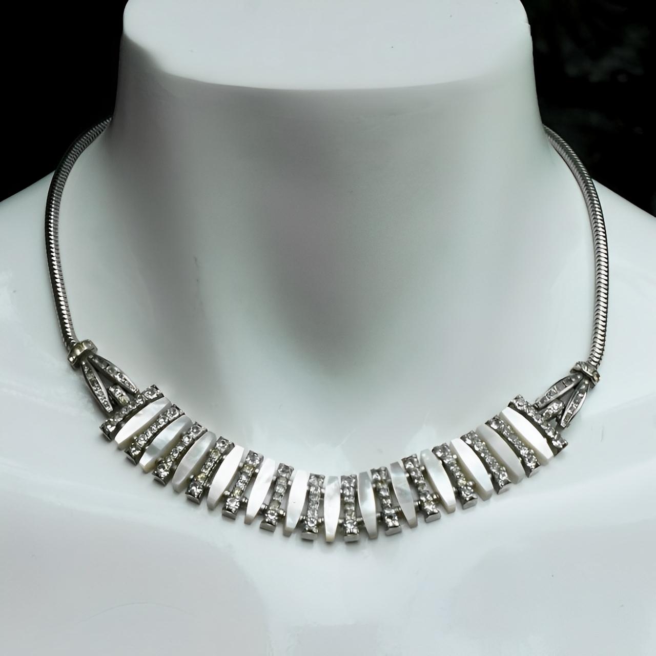 
Fabulous silver tone Art Deco necklace featuring rhinestones and mother of pearl. The rhinestones and mother of pearl are separated by metal beads, to create the curve to go around the neck. It is probably German, but is not stamped. There is wear
