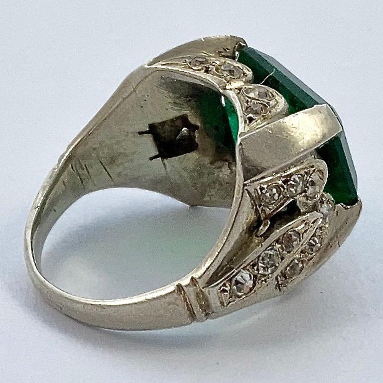 Art Deco silver ring, featuring a lovely emerald green paste stone in an open back setting, surrounded by clear paste stones. Circa 1930s. The ring is not stamped, but tests for silver. Ring size UK I, US 4 1/4, inside diameter 1.55cm. The green