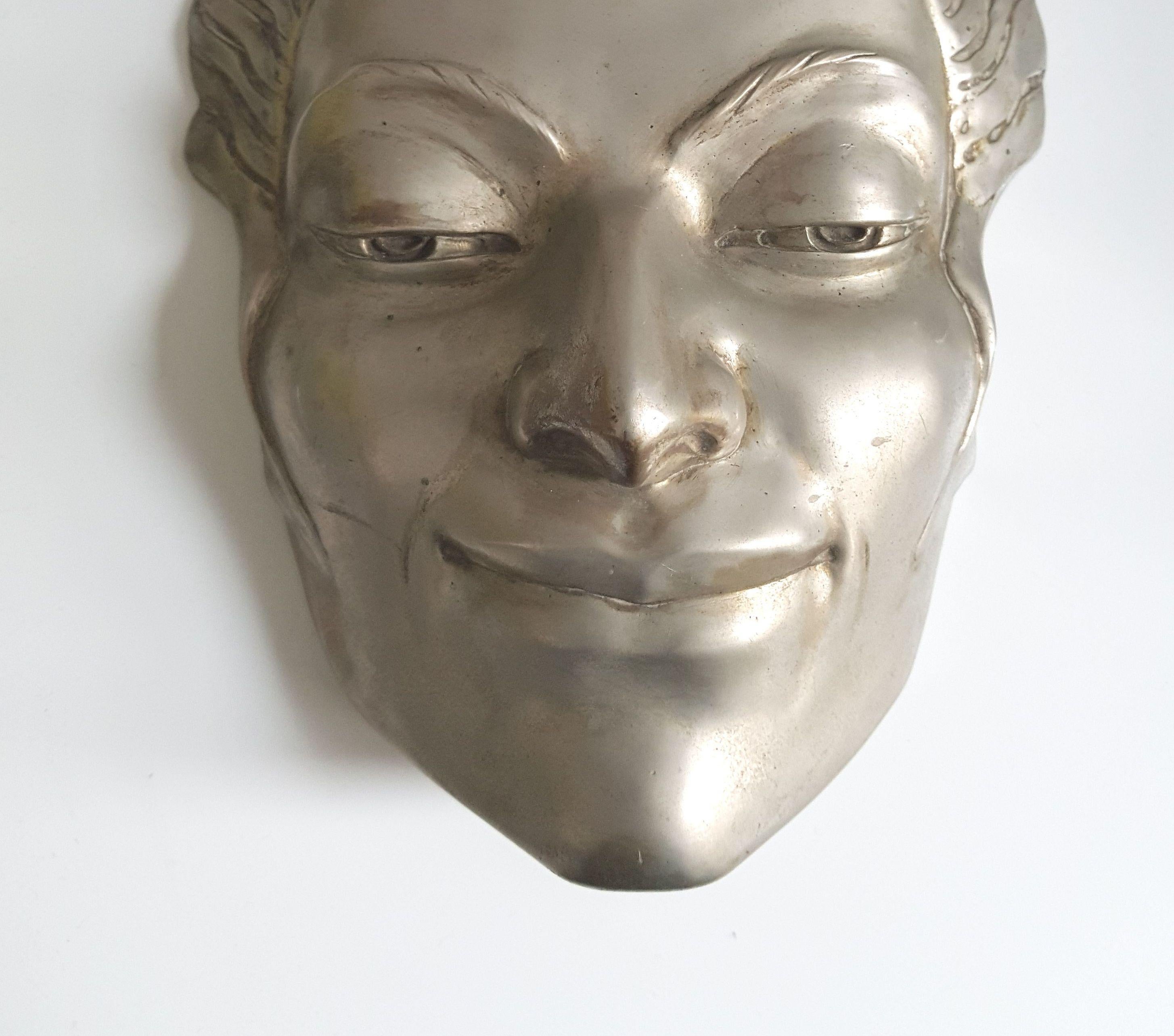 Versilberte Bronzemaske einer Frau, eine Originalarbeit von Doris Kathleen Flinn. Wahrscheinlich handelte es sich dabei um ihren Partner, der ihr oft als Modell diente. Er kann an die Wand gehängt, auf einen Ständer montiert oder sogar als markanter