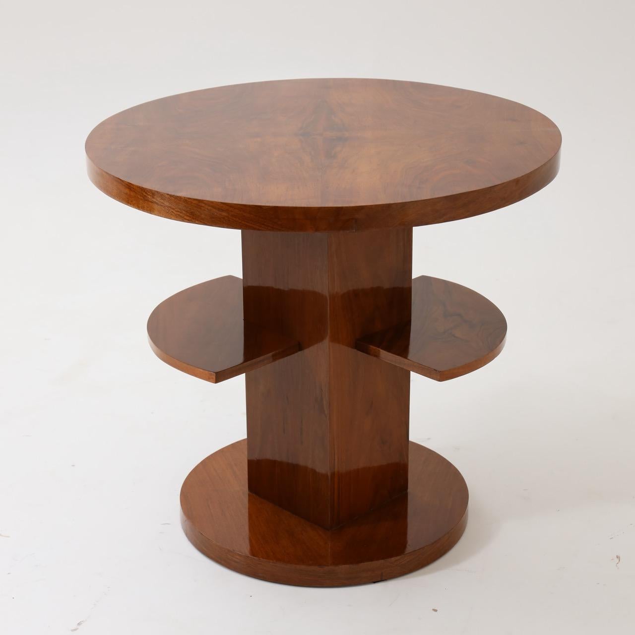 An Art Deco round side table. 
Walnut with central support featuring
two smaller shelves resting on a round base.