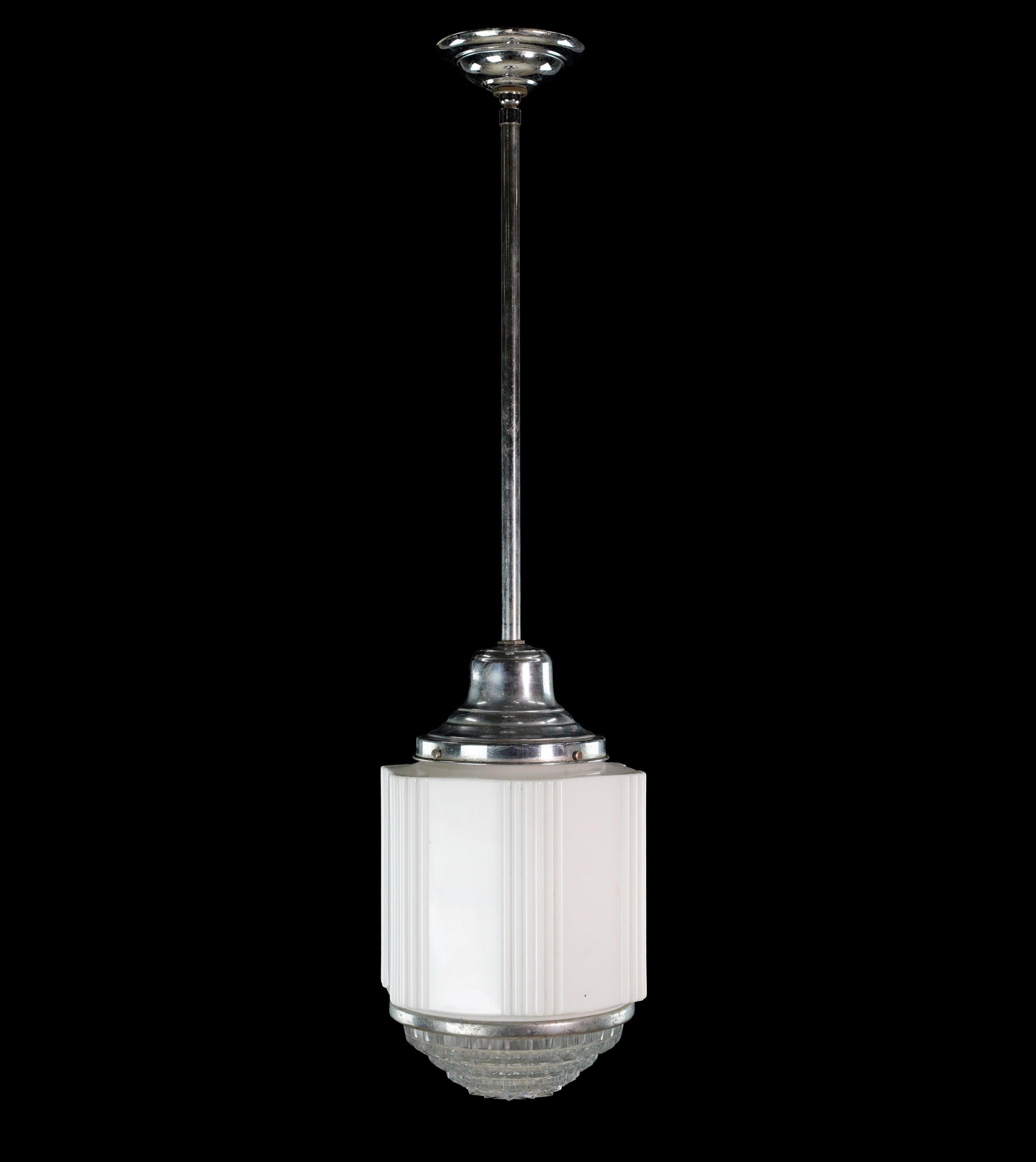 This Art Deco style skyscraper pendant light is attached to a nickel plated steel tube and canopy, with a fluted milk glass shade and clear bottom lens housing one standard socket. The Fresnel lens is held together by an adjustable silver ring.