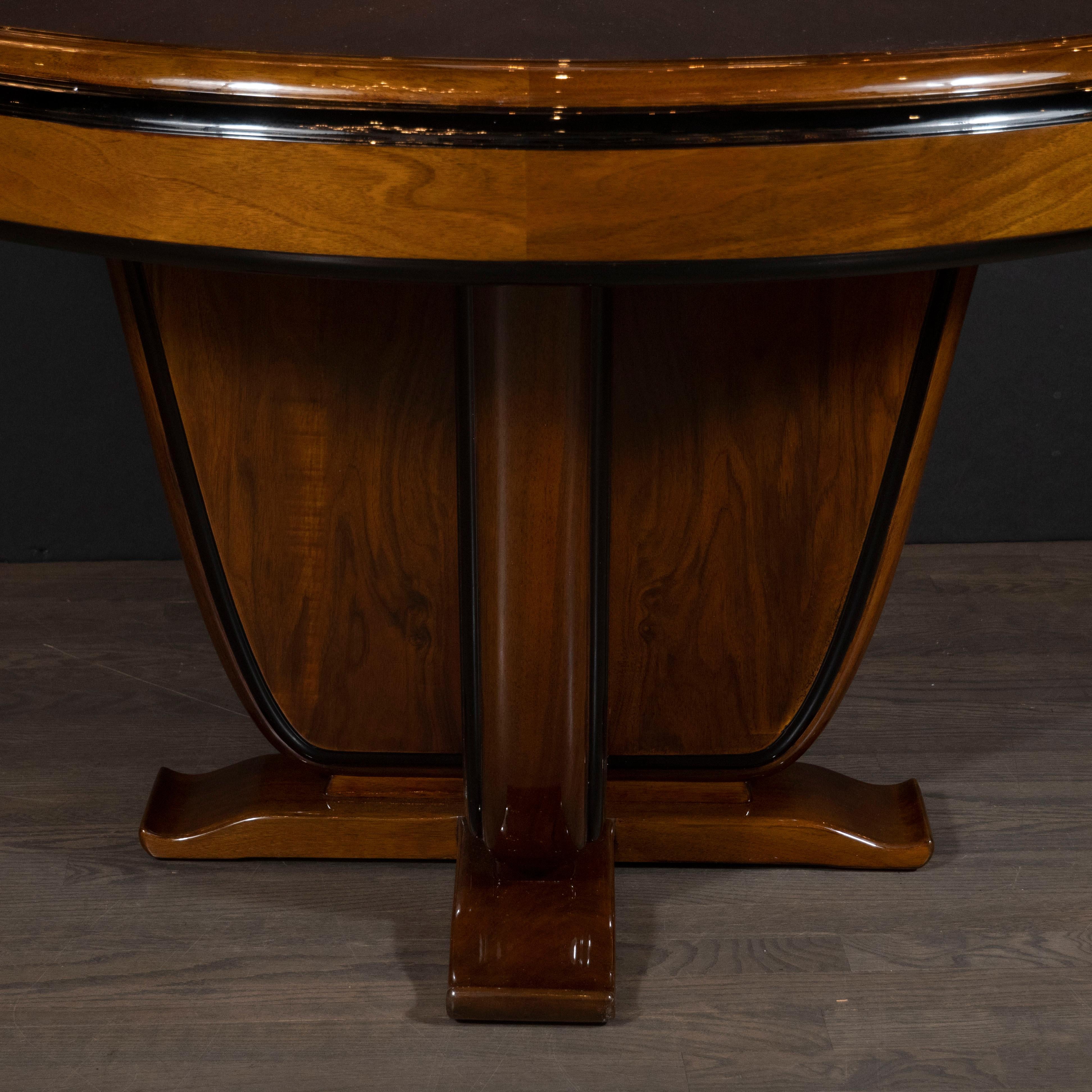 This refined Art Deco dining/centre table was realized in France, circa 1935. It features a three-tier black lacquer banded skyscraper style in bookmatched walnut with streamlined supports (also circumscribed in black lacquer) and undulating