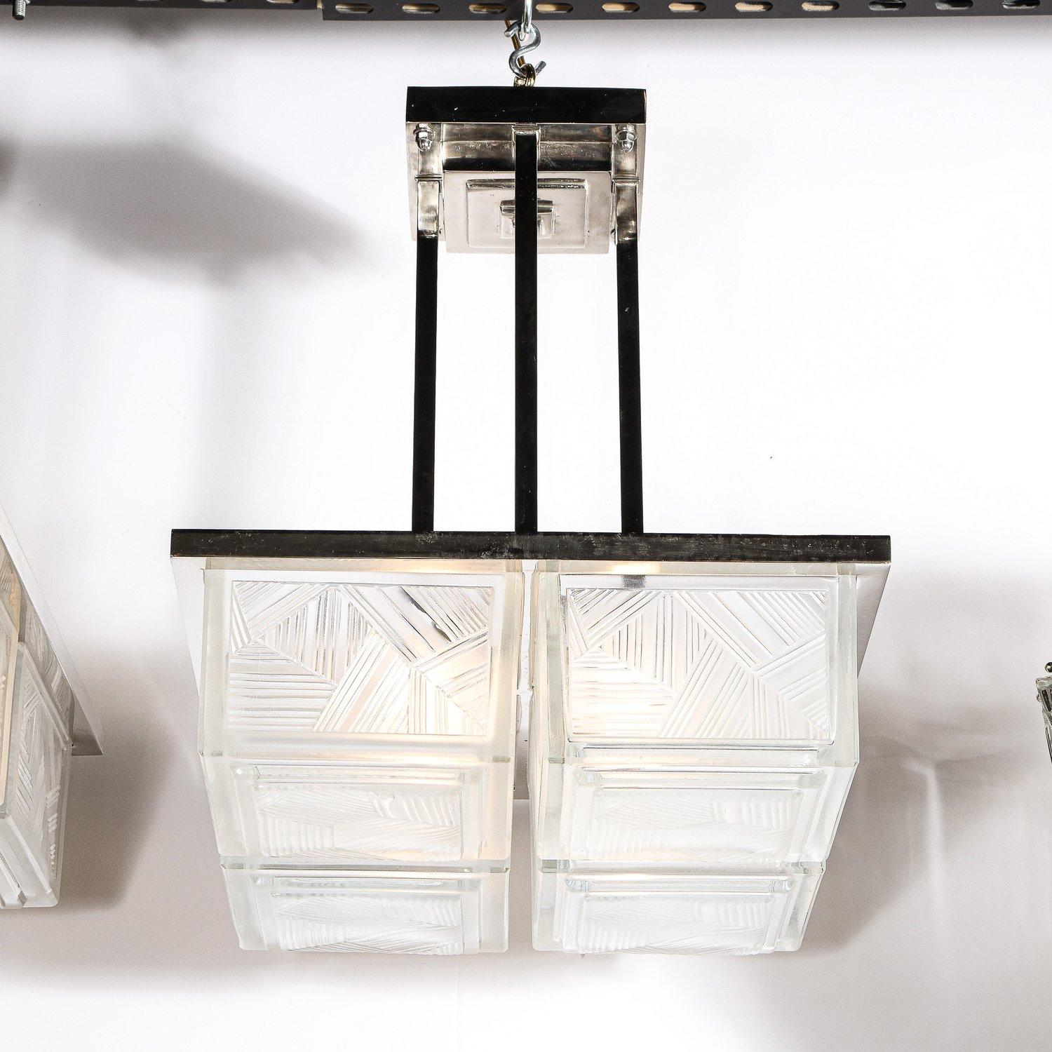 This rare and stunning Art Deco chandeliers were realized by the illustrious atelier of Sabino in France circa 1930. The chandelier features four separated volumetric cubic frosted glass forms with striated etched geometric detailing that attach to