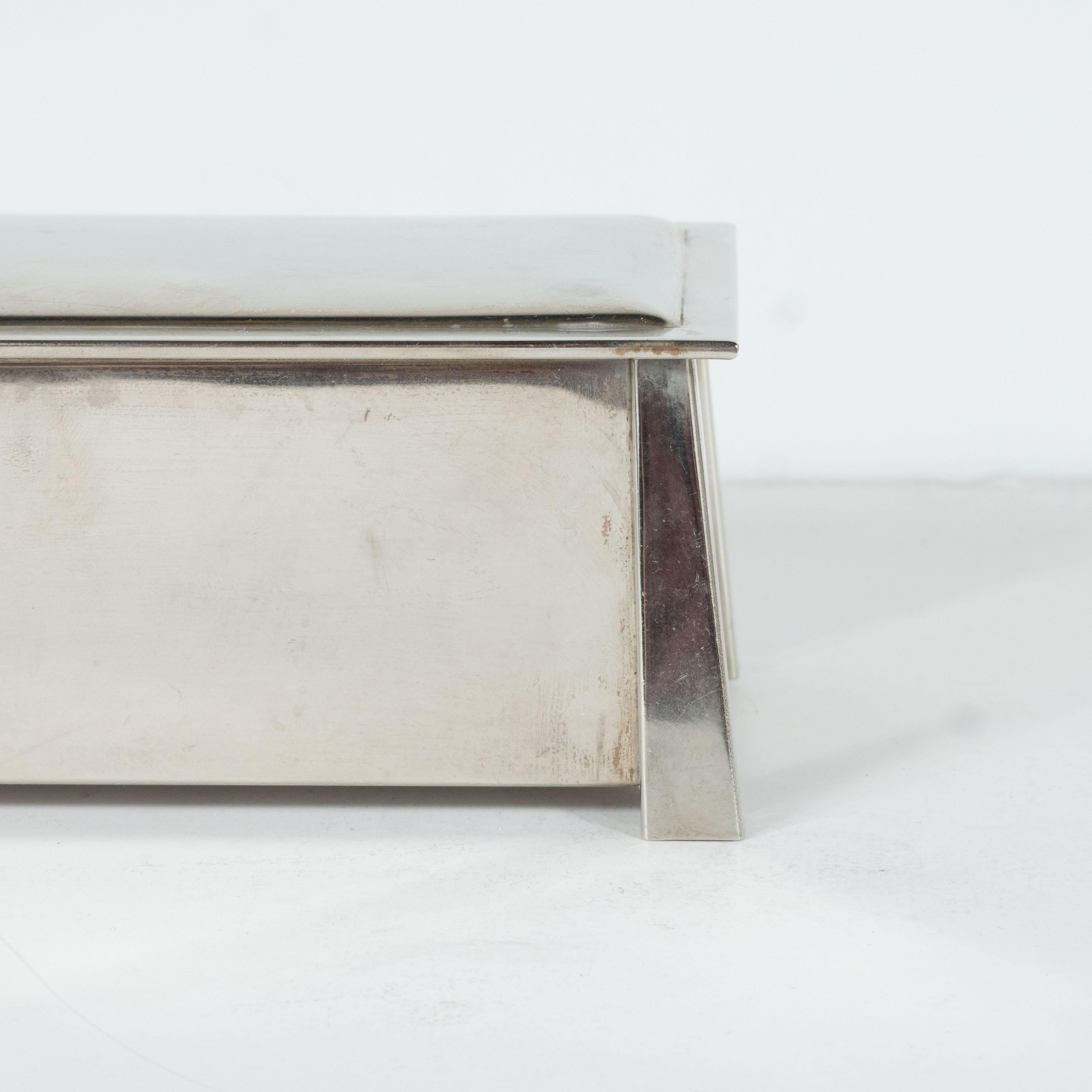 This elegant Art Deco Machine Age box was realized by the renowned silversmith studio L. & M.T. Co. in the United States, circa 1935. It features a subtly convex two tier skyscraper style rectangular top that peaks over the volumetric tapered
