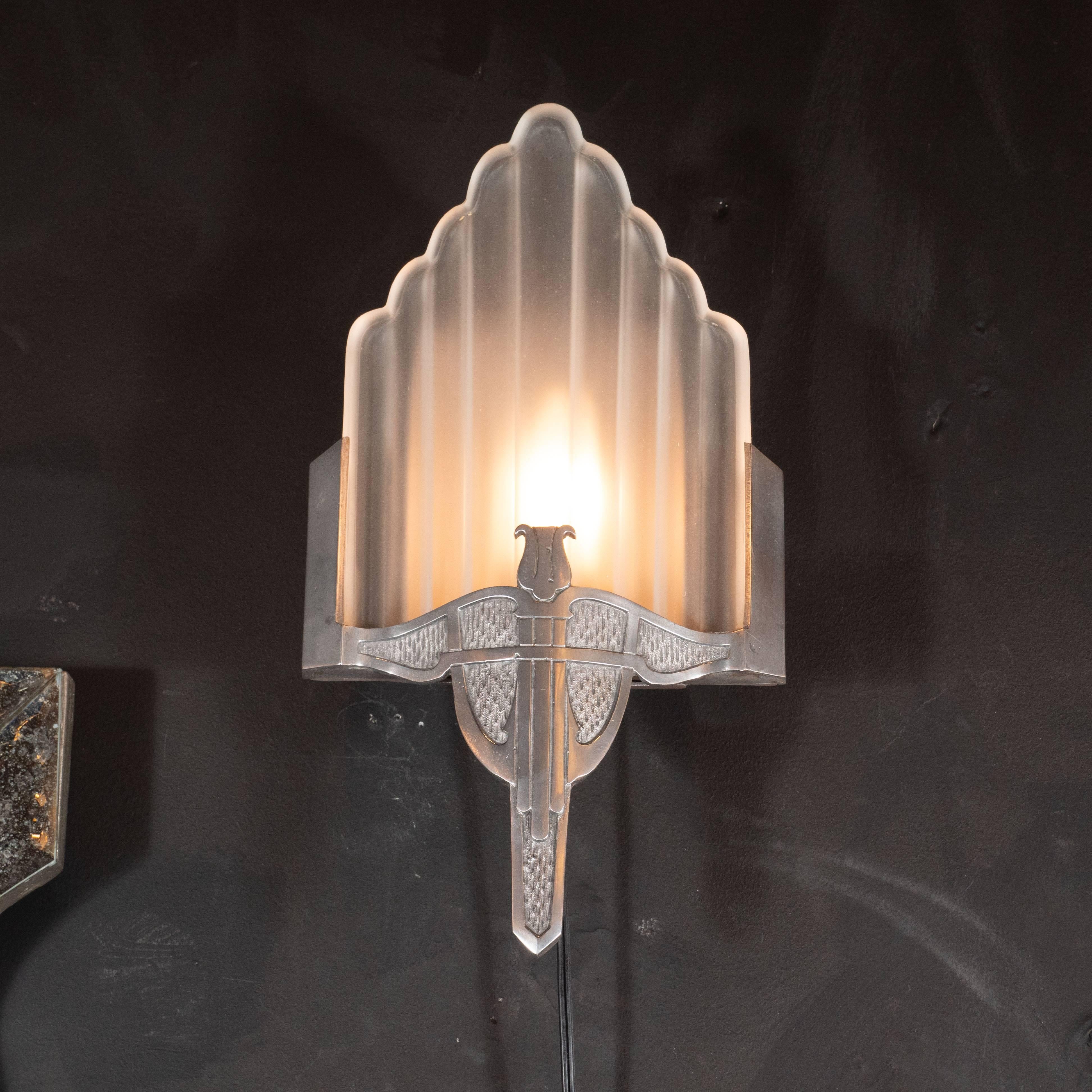 This gorgeous pair of Art Deco Machine Age sconces were realized in America, circa 1935. They feature nickelled bronze bodies with a stylized harp motif in the centre surrounded by a flecked pattern, imbuing the piece with a dynamic sense of depth.
