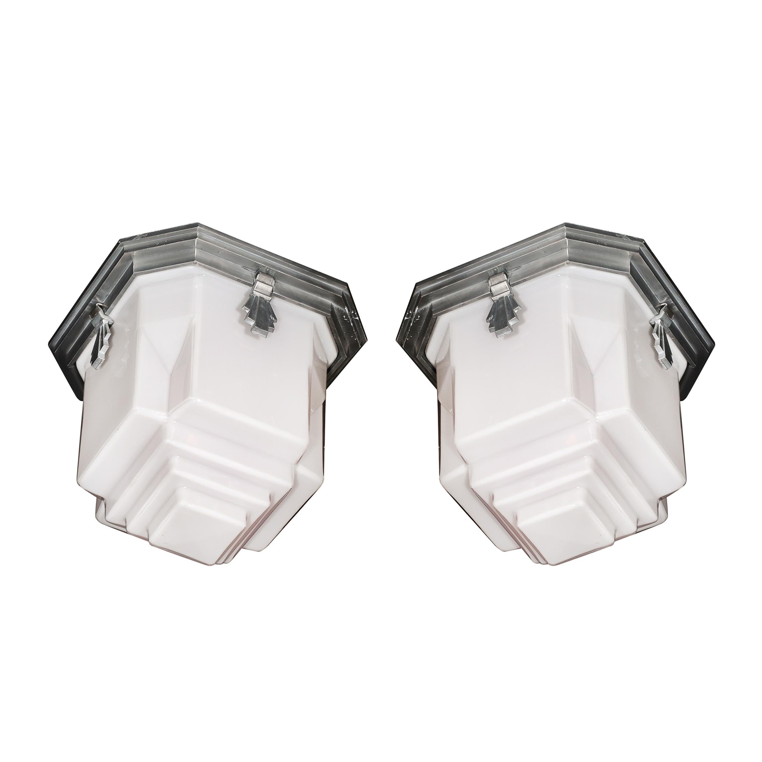 Cette paire exceptionnelle de lustres encastrés de style Skyscraper Art Deco reflète l'élégance géométrique emblématique de l'époque. Originaire des États-Unis vers 1935, chaque luminaire est doté d'un abat-jour en verre au lait moulé avec des