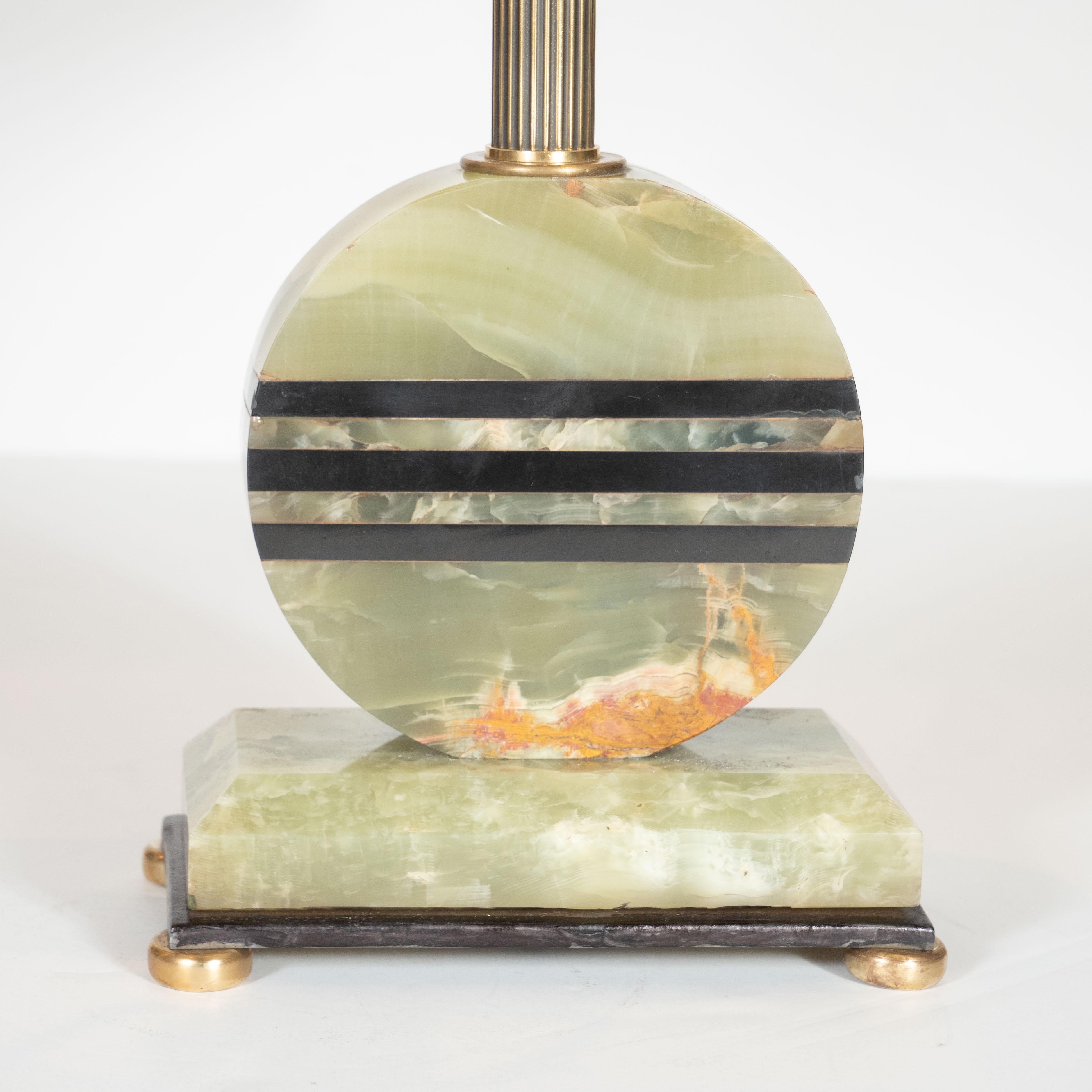 This elegant Art Deco Machine Age table lamp was realized in the United States circa 1930. It features a skyscraper style base sitting on four circular streamlined antique brass feet that support a bronze tier. A layer of green onyx rises from the