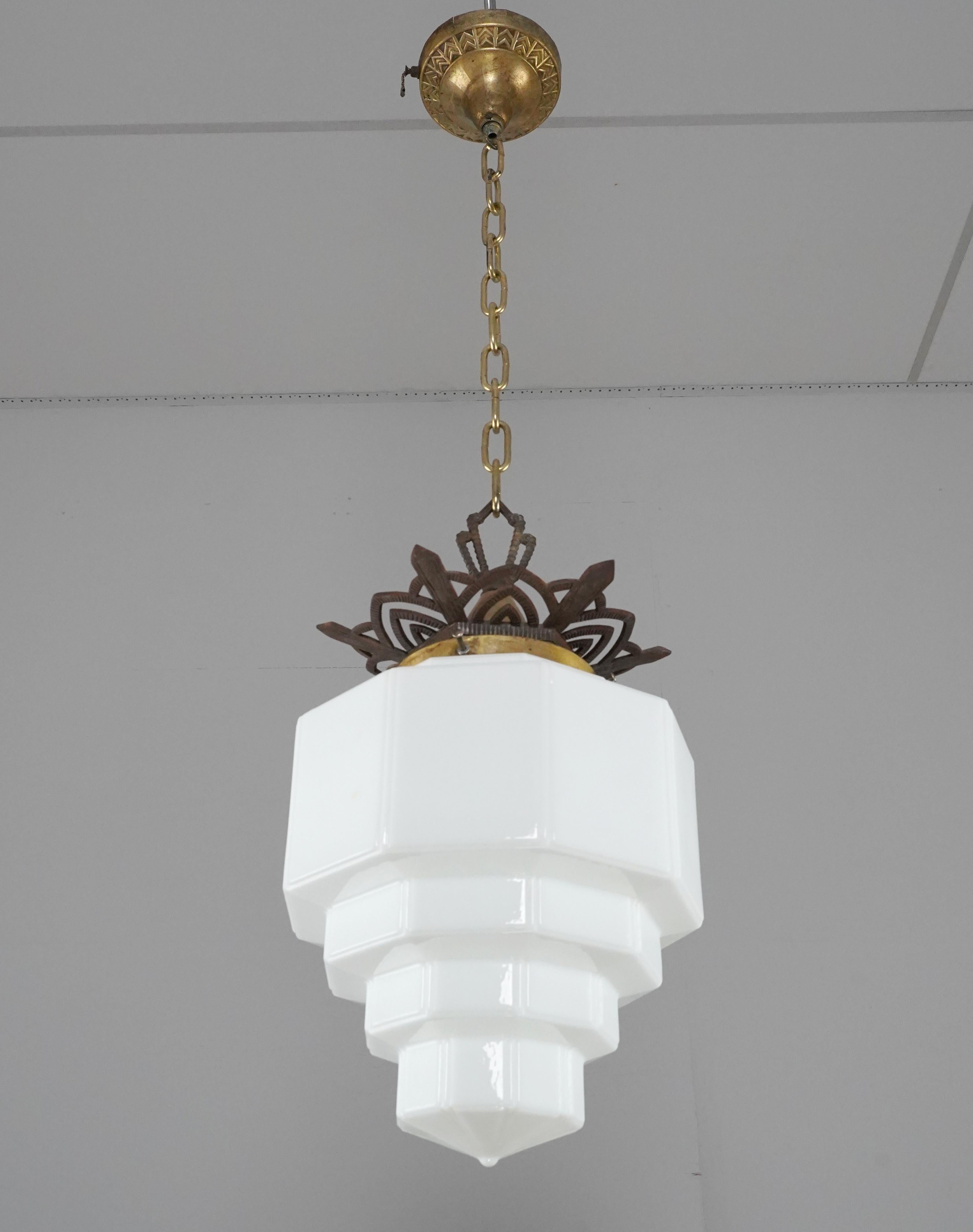 Art Deco style skyscraper pendant light with a multi-tiered white milk glass globe and cast iron and brass ornate chain fitter. The canopy has a small crack in it. This requires one standard Edison style medium base bulb. Cleaned and restored. Good