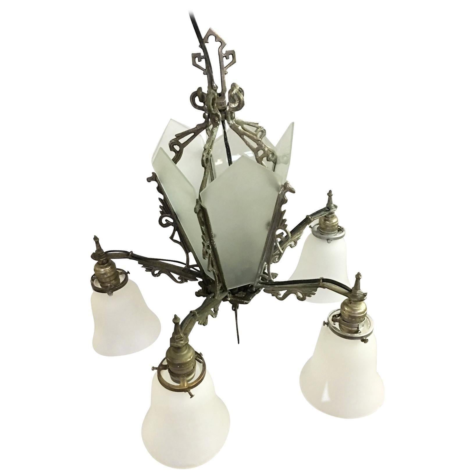 Lustre géométrique Art Déco à cinq branches avec cinq lampes suspendues avec des abat-jours en forme de cloche et un centre en verre opale à lamelles éclairantes. La pièce est ornée de détails en forme de volutes, tandis que la base du lustre est
