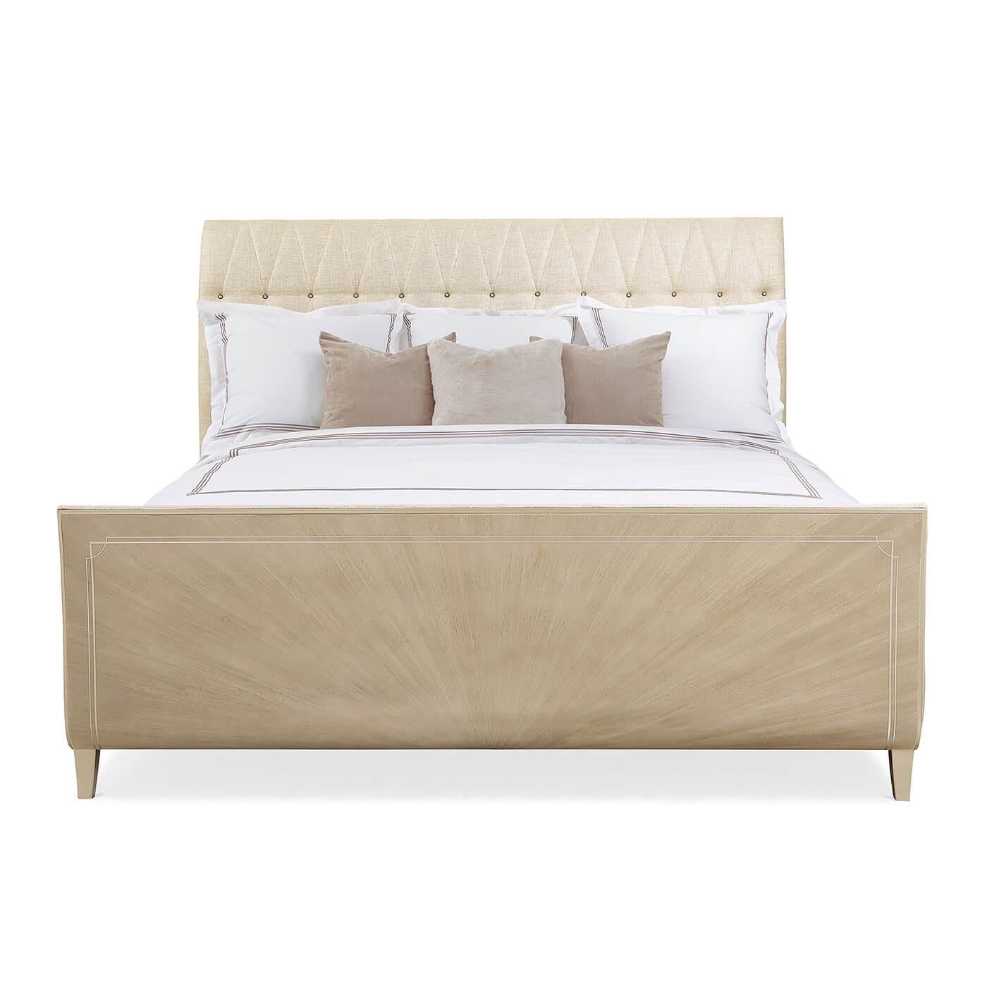 An Art Deco-Style sleigh bed with an upholstered headboard featuring a diamond tufted pattern with glass buttons. It has a curved footboard crafted with a stunning Koto veneer in a radiating fan pattern in our Winter Wheat finish. Its curved feet