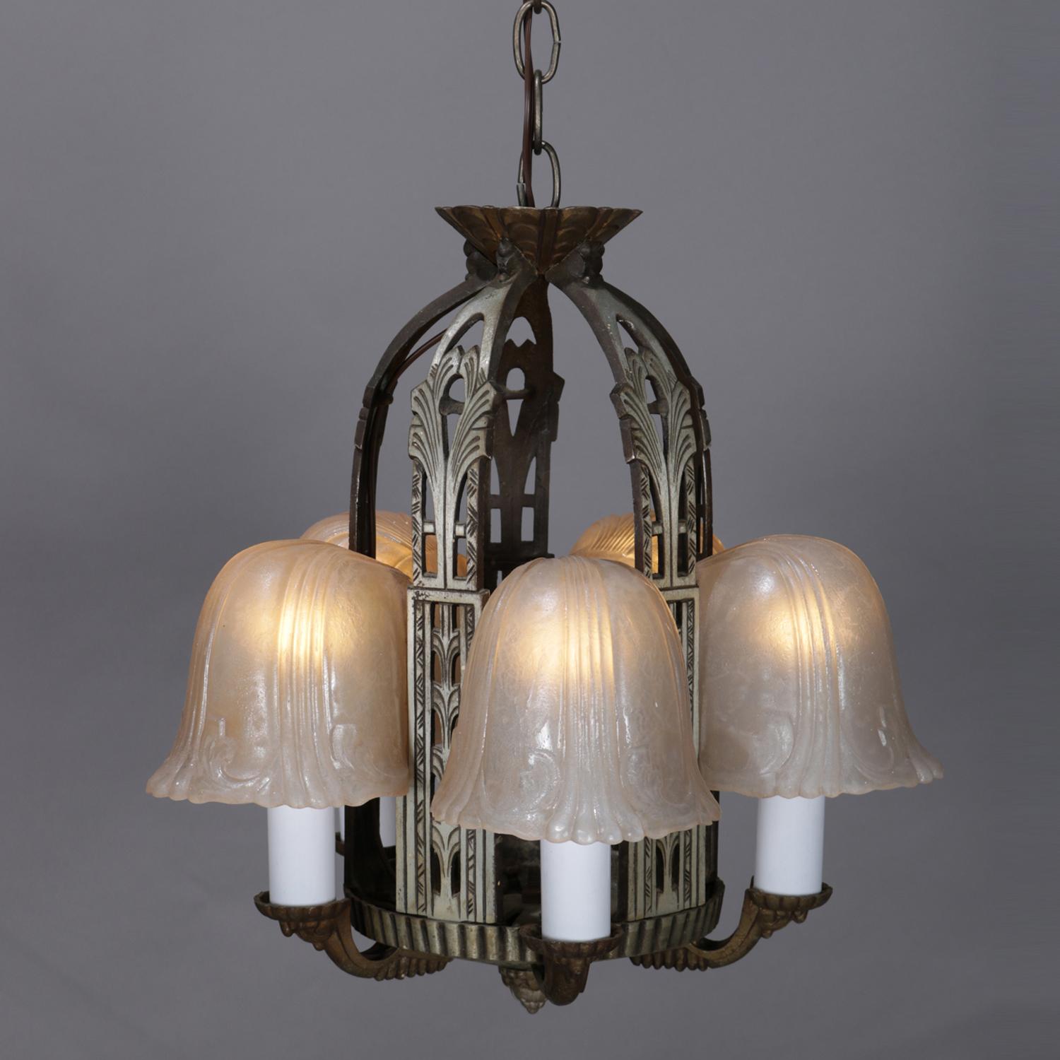 An Art Deco chandelier features cast cage form frame with incised stylized foliate decoration and five arms terminating in candle lights with art glass slip shades, professionally rewired, circa 1930.

Measures: 32