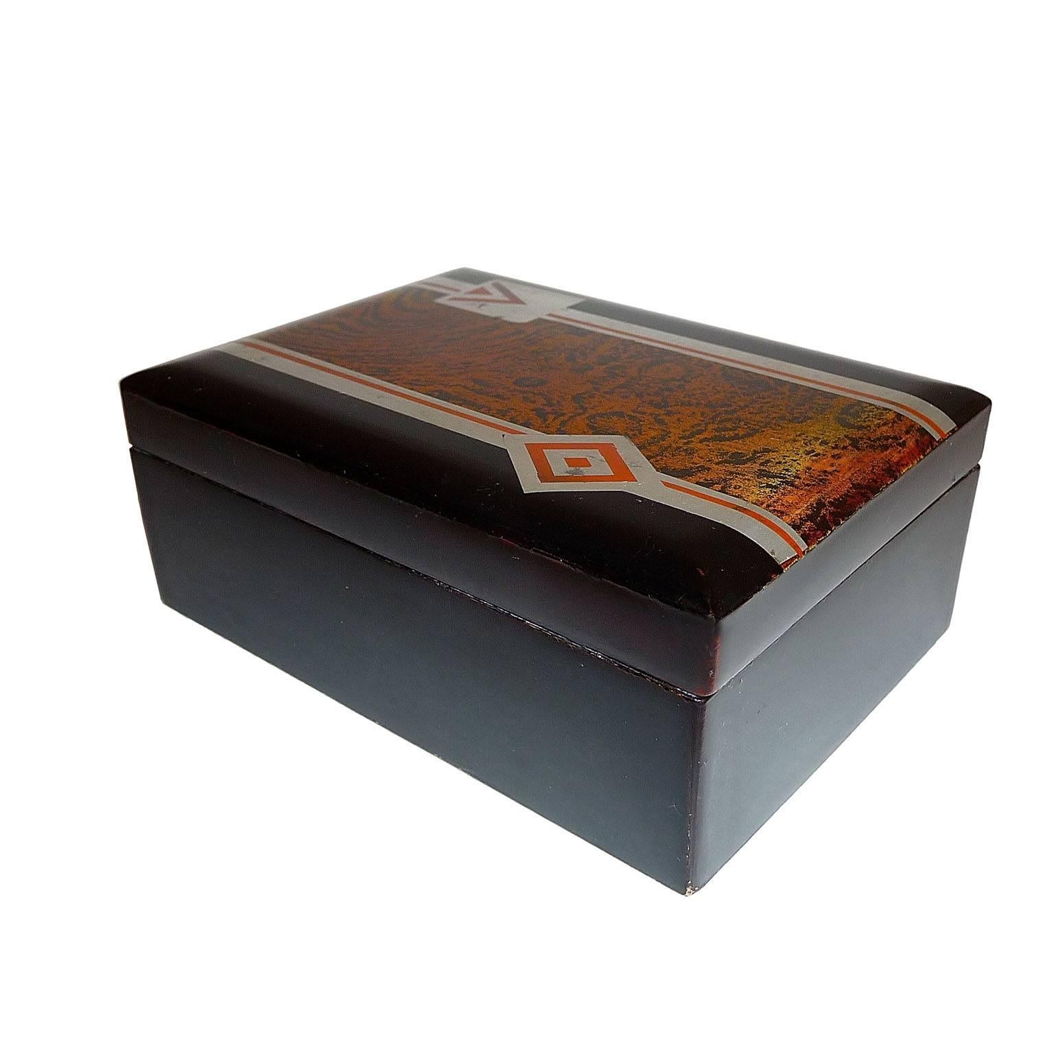 Art Deco small lacquered box, France, circa 1930.
Very beautiful box, black lacquer. Lid decorated with geometric design in silver leaf and light red lacquer, against a wood imitation background.
Dimensions:
12 x 9 x 4.5 cm (4.73 x 3.54 x 1.77