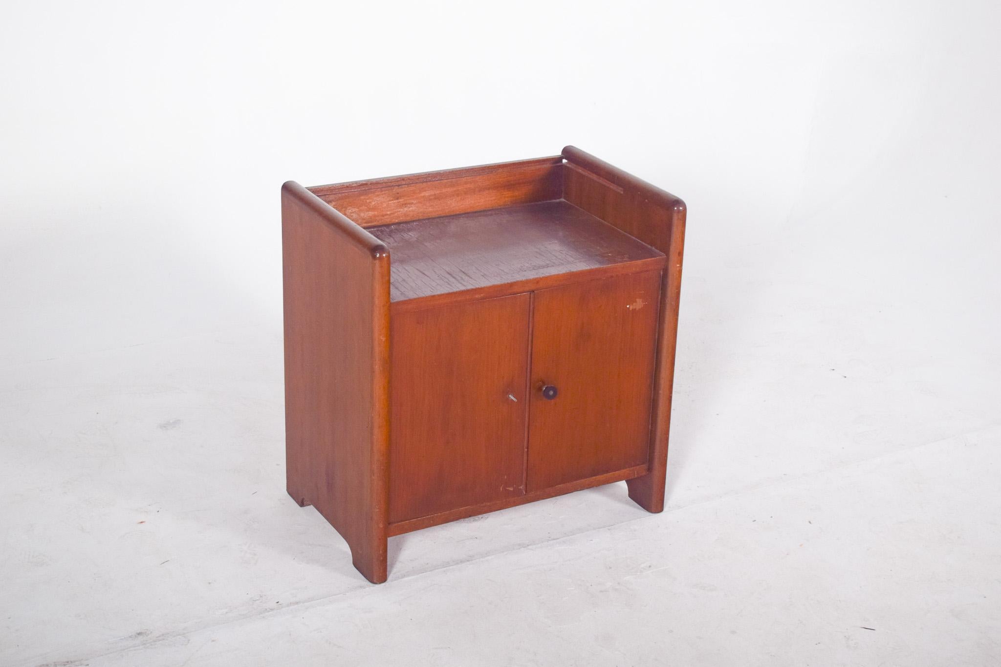 Teak bar cabinet.  With a compact and functional design, the cabinet has a rectangular structure with rounded sides and a satin varnish finish, which enhances the warm tone and natural grain of the wood. At the bottom, two front doors with side