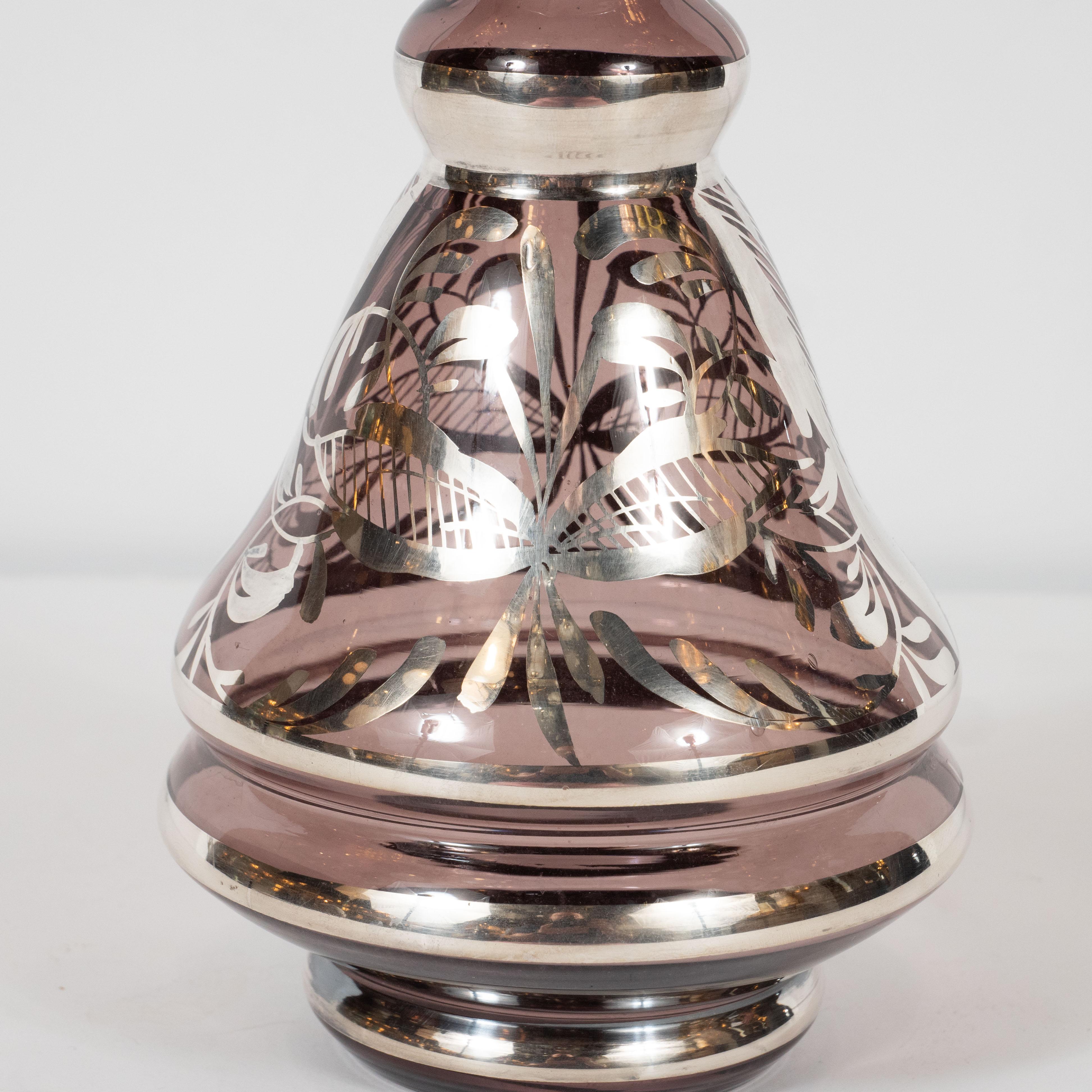 This gorgeous Art Deco decanter was realized in Czechoslovakia, circa 1930. It features a tiered skyscraper style base whose edges are finished with sterling silver, and a conical body in smoked amethyst glass. The neck features sinuous curves that