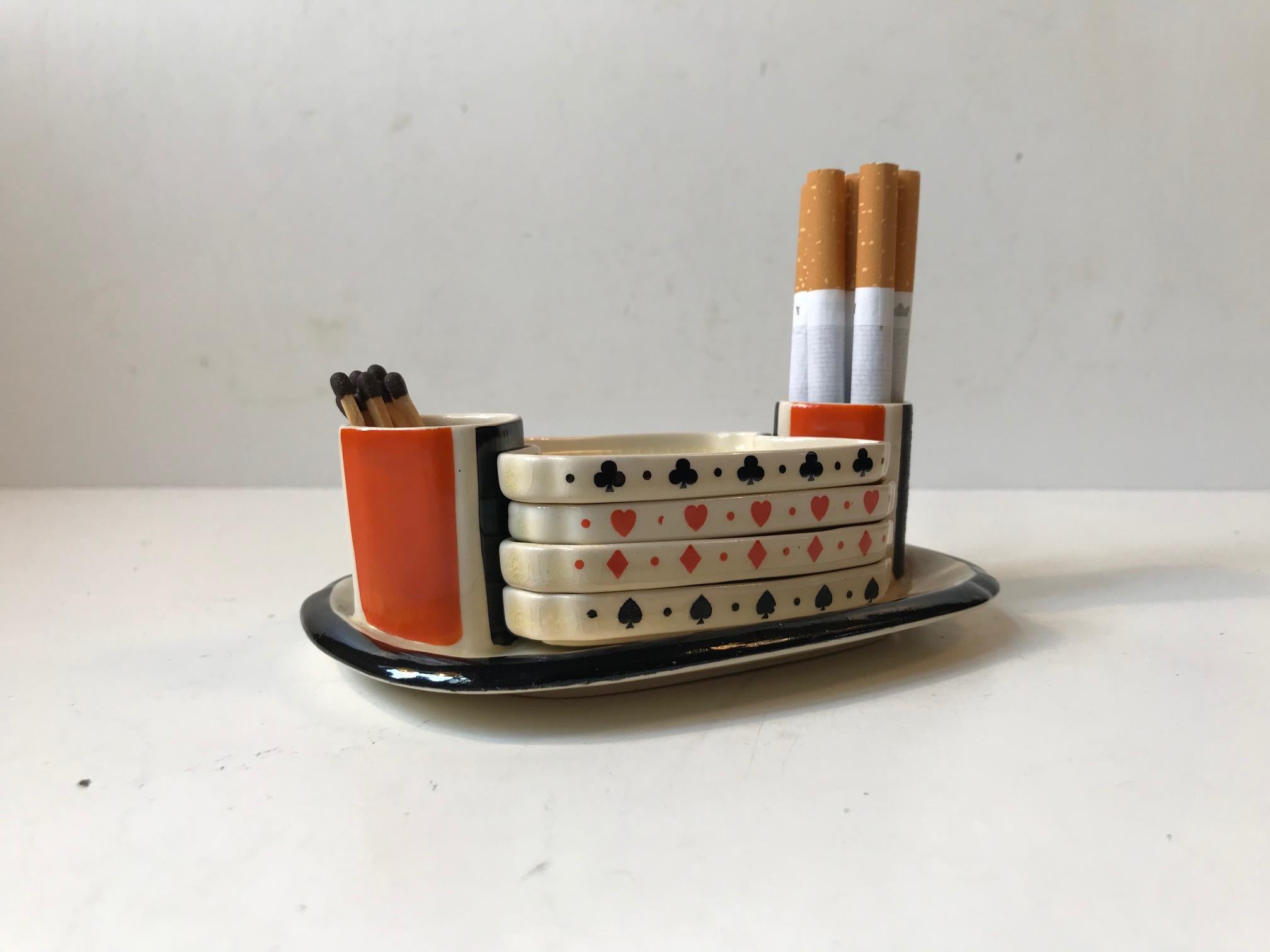 Unusual yet practical novelty item from Royal Doulton, England circa 1930. A set of 4 ashtrays, each with a card suit on it: diamonds, club, spades and hearts - which all fit neatly onto a china holder. On each side of the holder are red and black