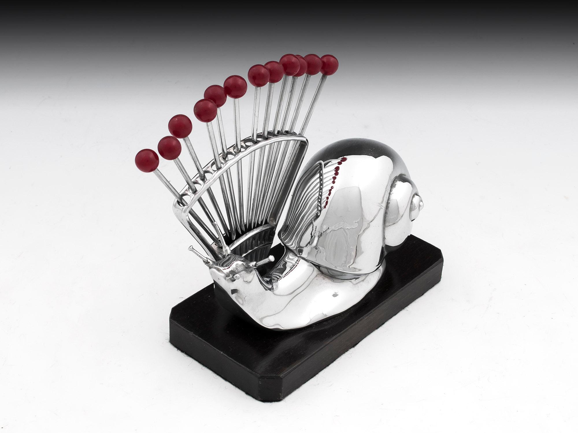 Art Deco chromium plated cocktail stick holder in the form of a snail. Containing twelve cherry topped cocktail sticks, standing on a ebonized plinth.