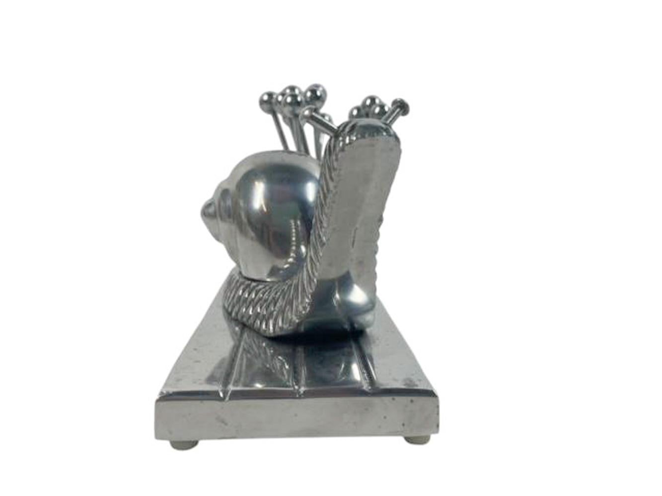Juego de púas de cóctel Art Decó de aluminio pulido diseñadas como un gran caracol sobre una base rectangular con un soporte cilíndrico con 12 púas bifurcadas con punta de bola.